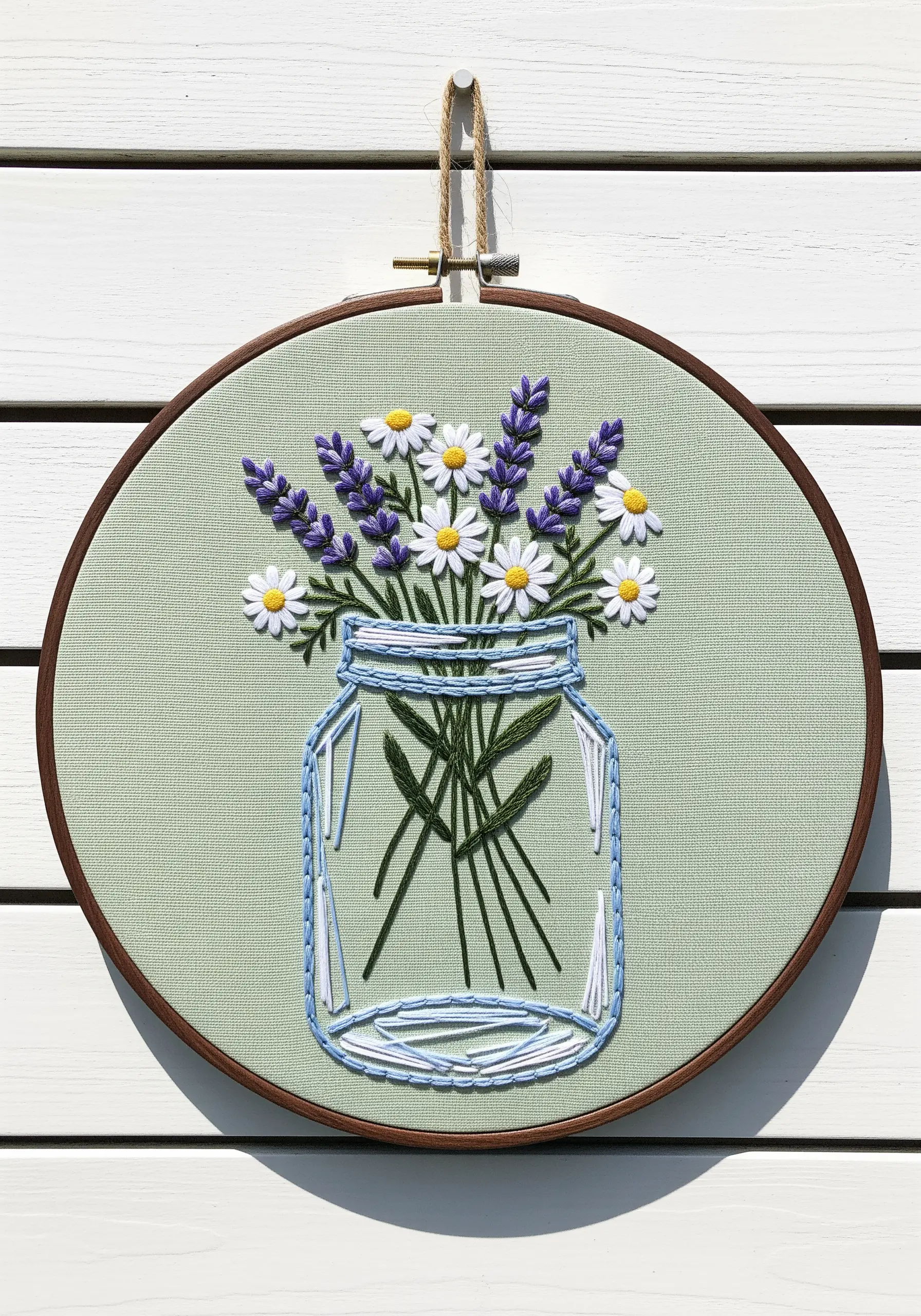 Embroidered daisies and lavender in a clear line-art jar on sage green fabric.