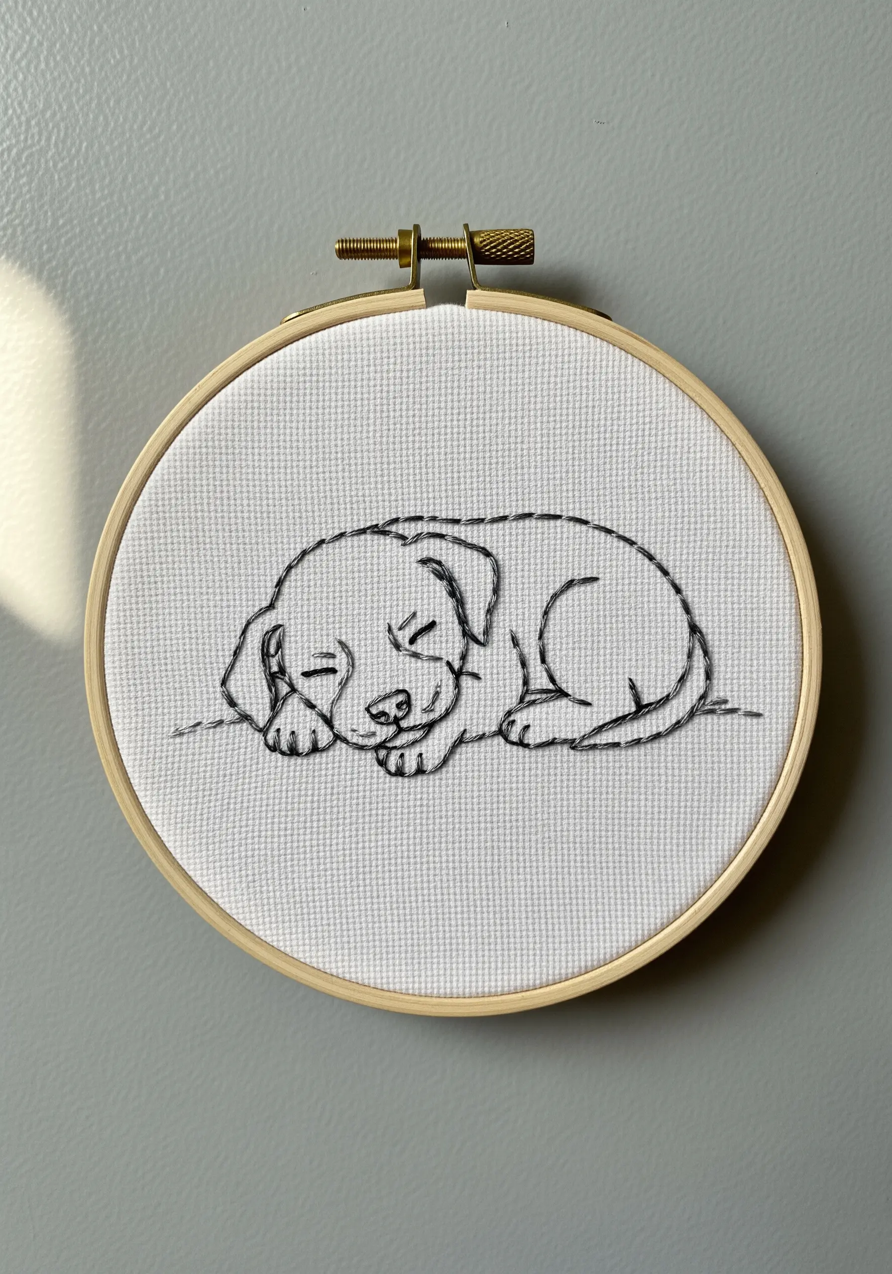 A delicate line art embroidery of a sleeping puppy on white Aida cloth.