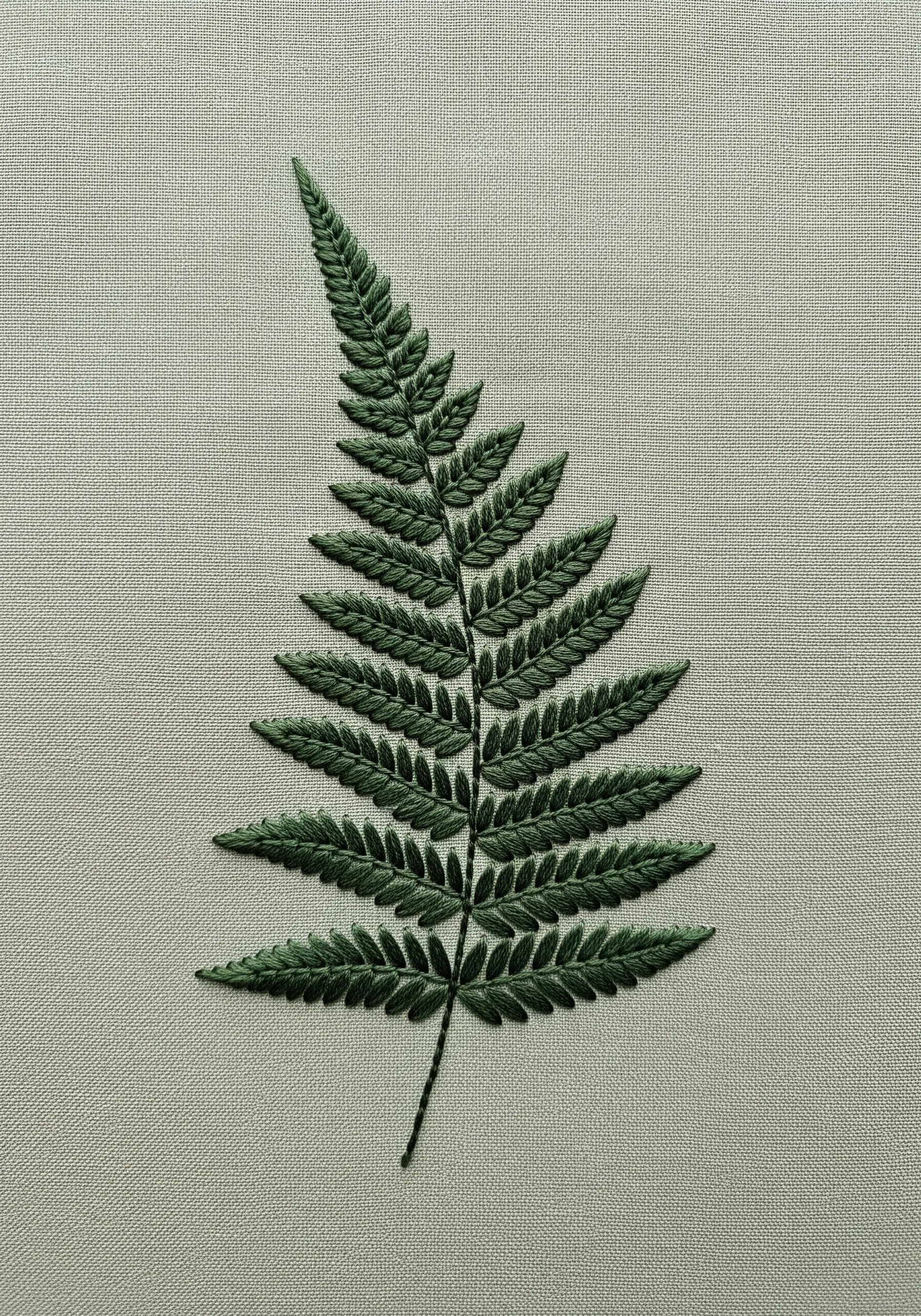 A detailed, realistic fern leaf embroidered in dark green thread on a light green fabric.