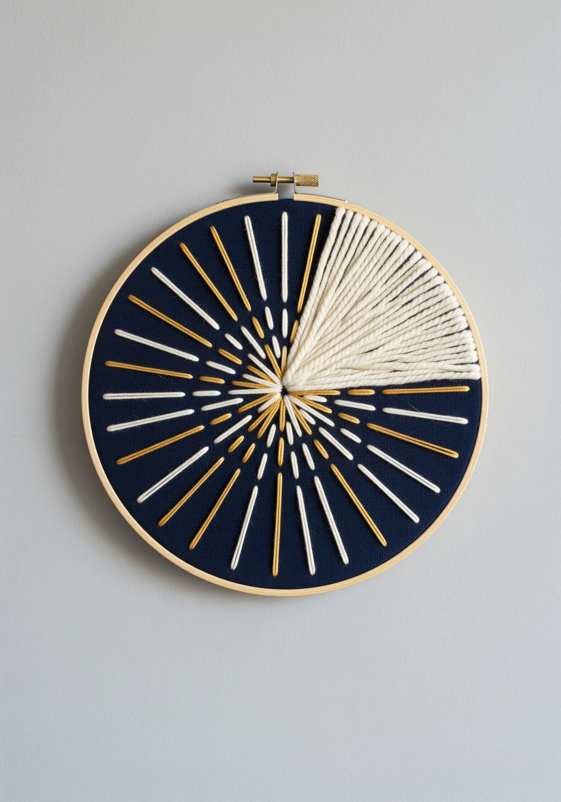 Abstract sunburst embroidery in a hoop using thick yarn and fine metallic threads on navy fabric.