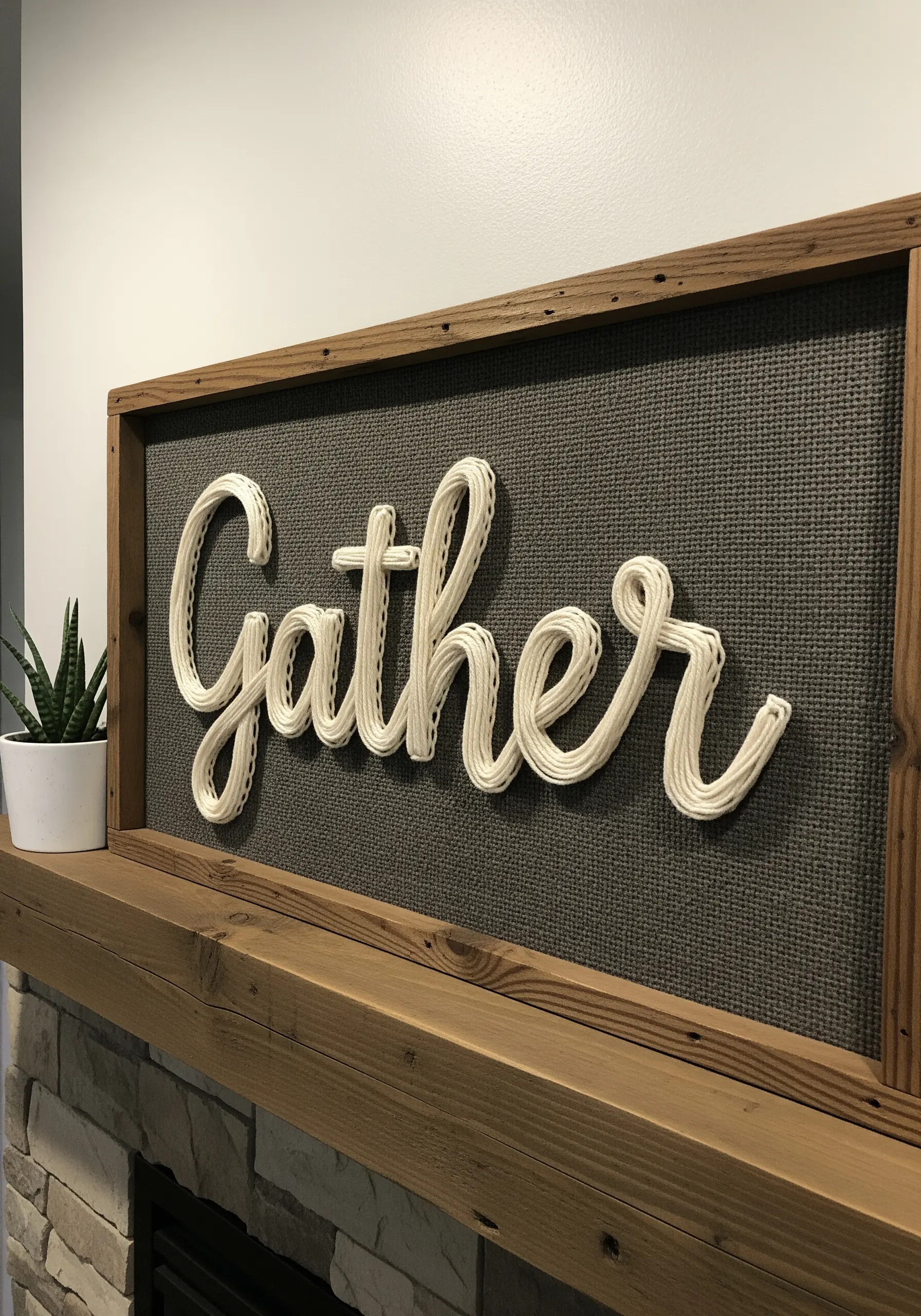 Thick white yarn couched in cursive script to spell 'Gather' on a textured gray background.