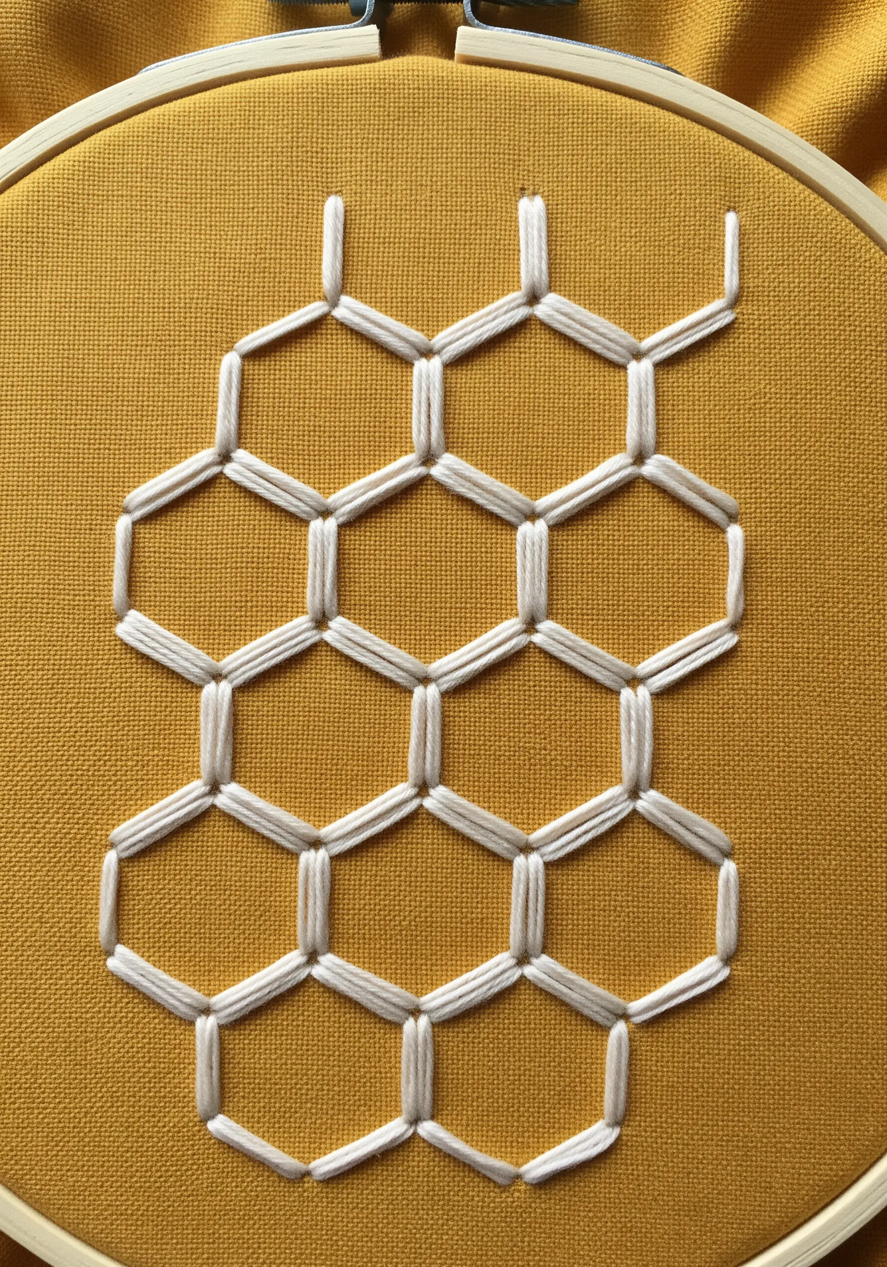 A geometric honeycomb pattern embroidered in white thread on a solid mustard-yellow fabric.