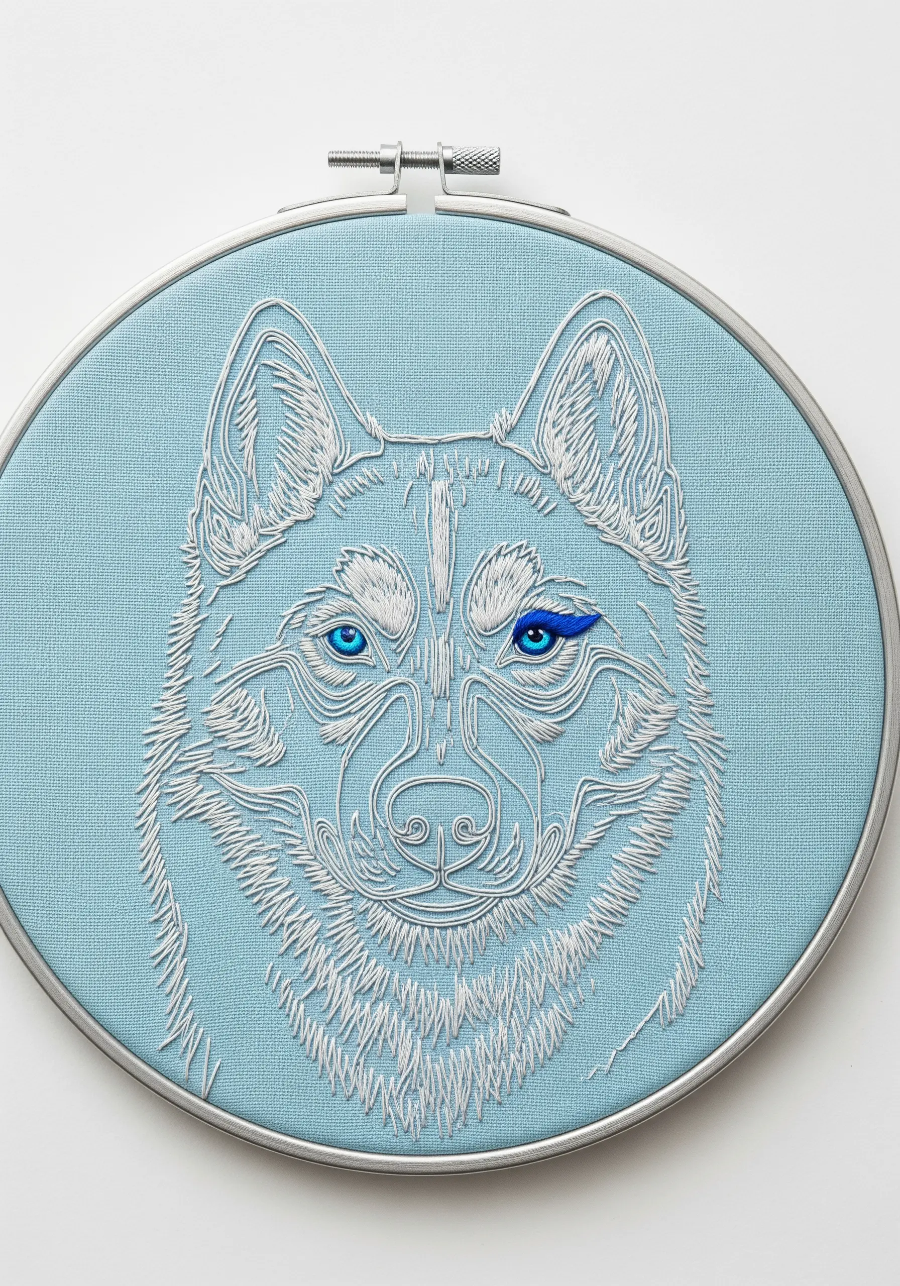 A husky portrait stitched in white on blue fabric, with intensely vibrant blue eyes.