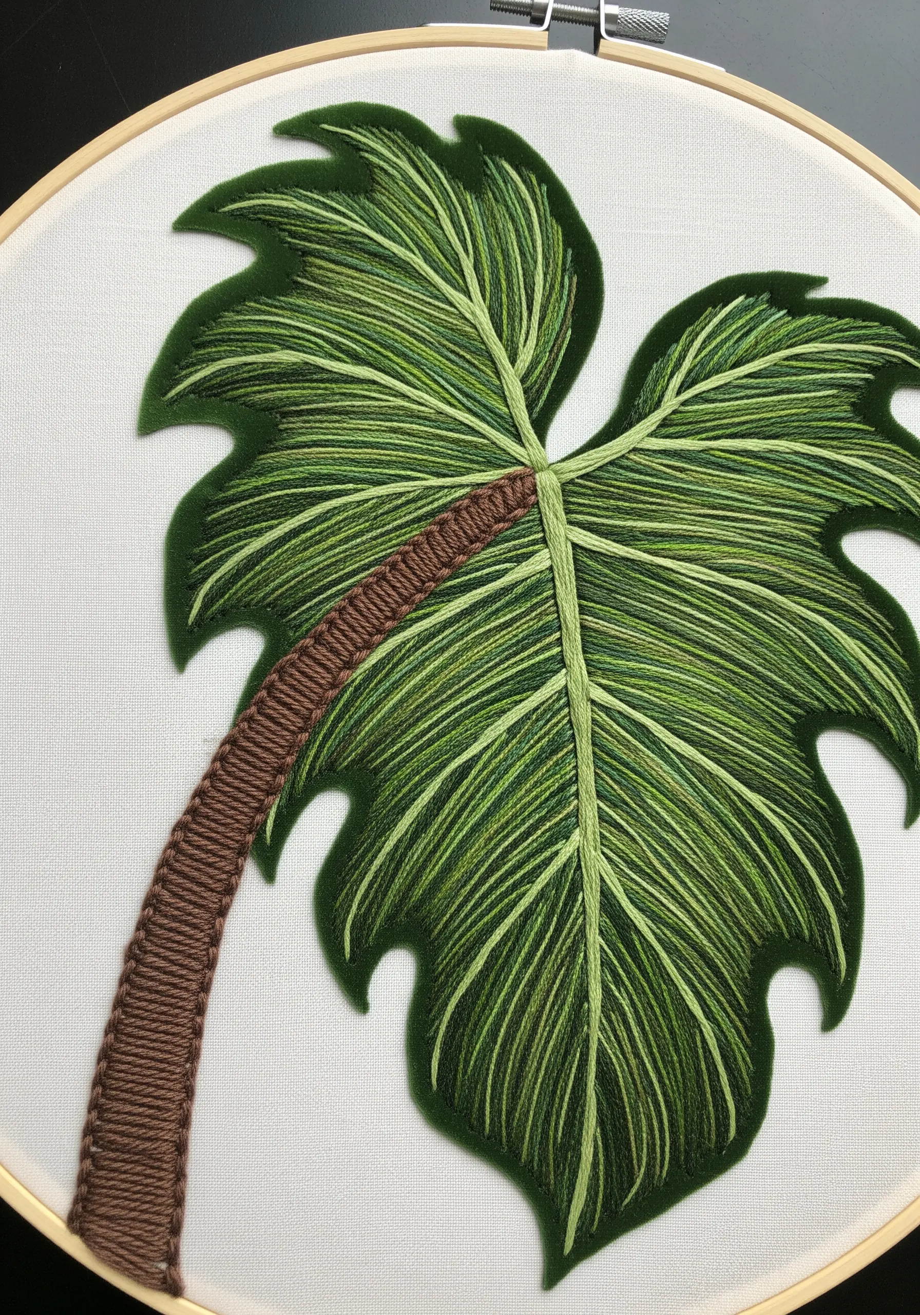 Detailed thread-painted embroidery of a green philodendron leaf with a raised brown stem.