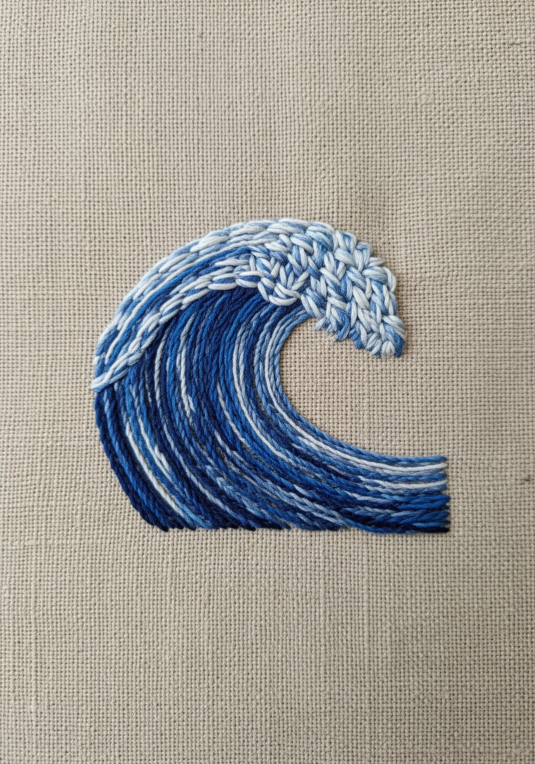 An embroidered ocean wave with blues and whites, featuring textured stitches for the foamy crest.