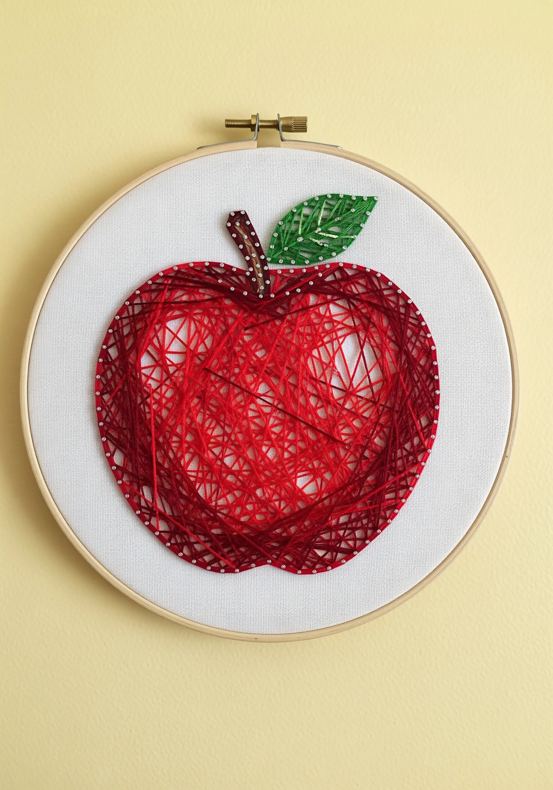 An apple silhouette filled with a web of red thread, contrasted by a solid green stitched leaf.