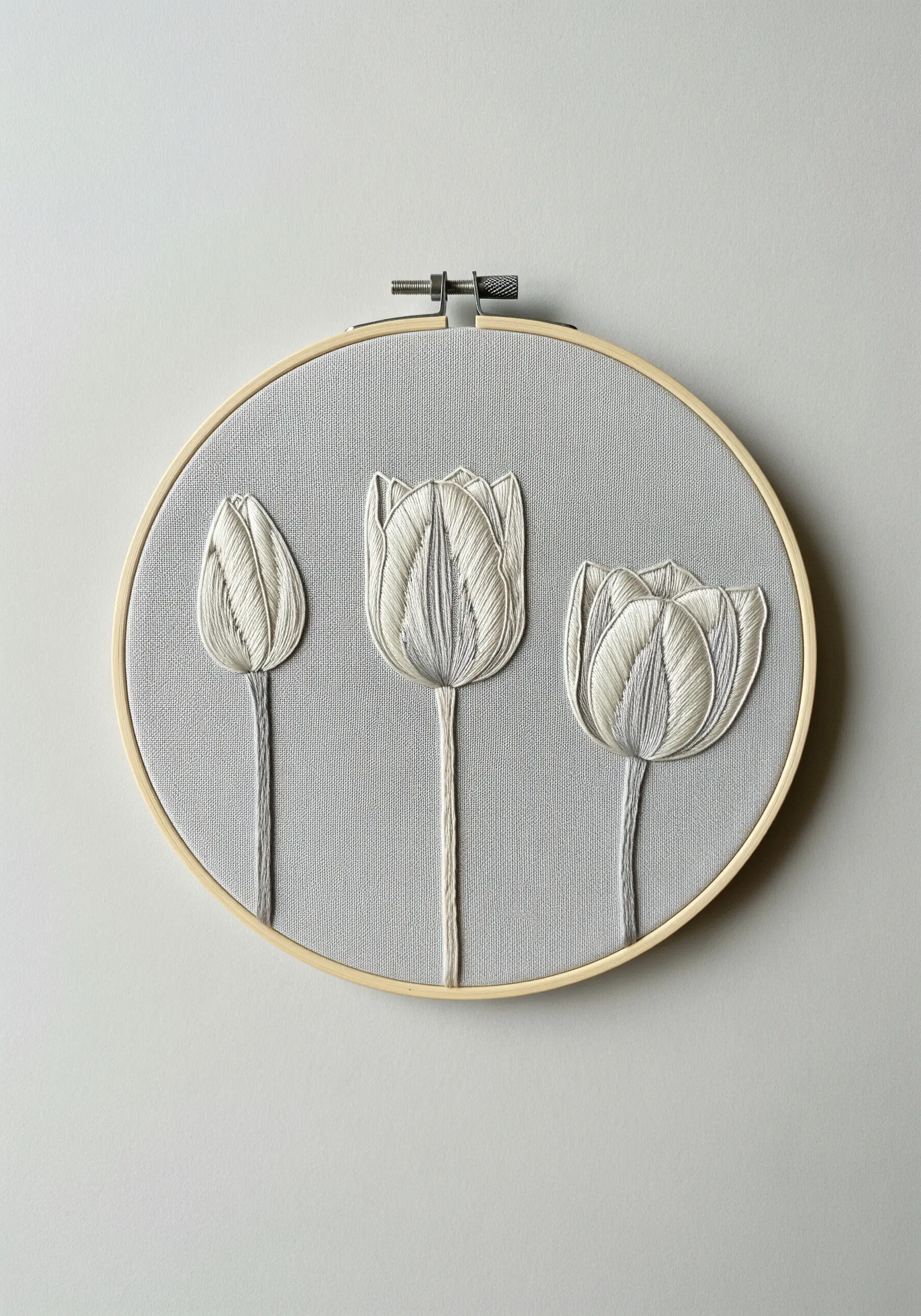 Three minimalist white tulips outlined and shaded with white thread on a grey canvas.