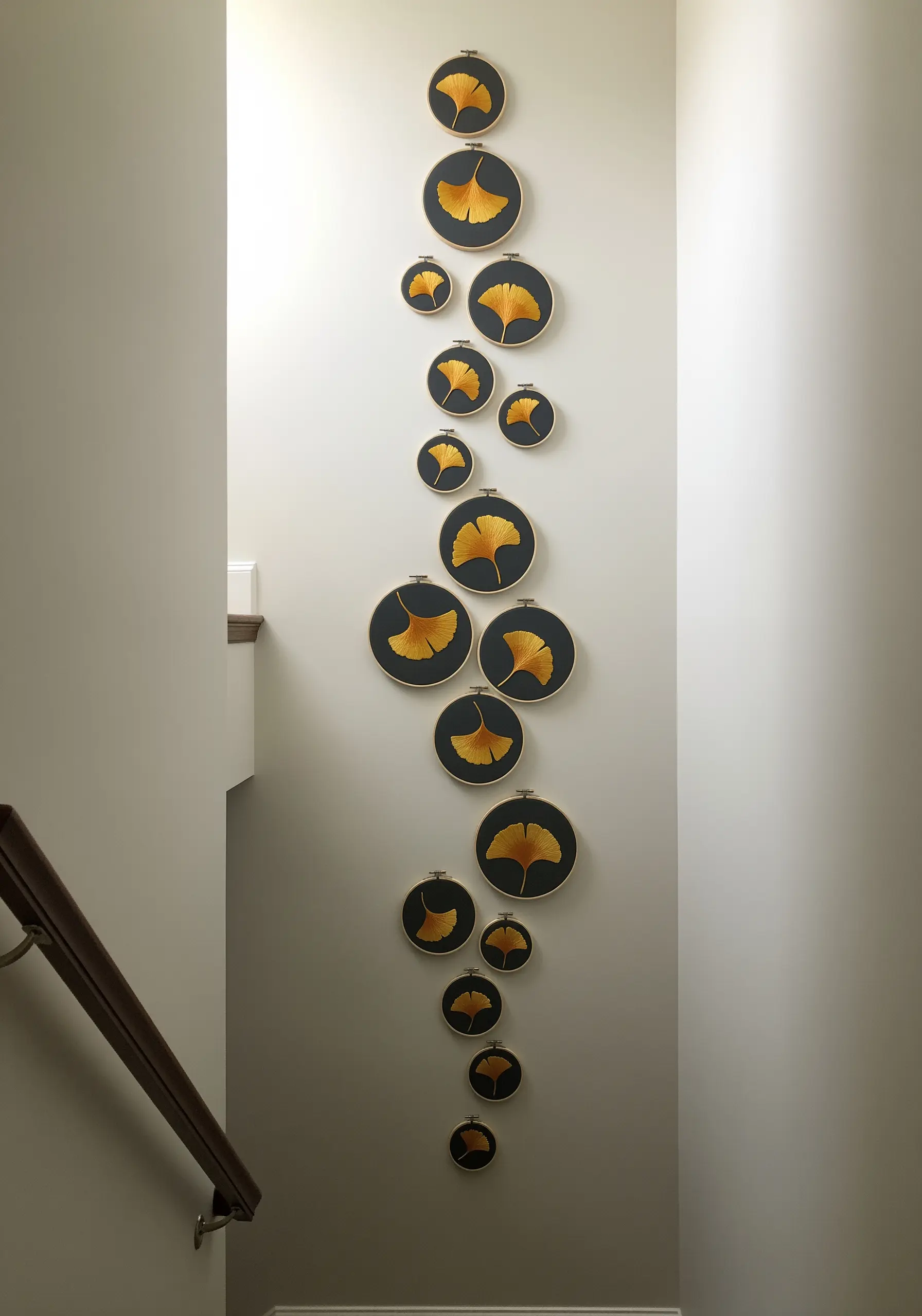 A vertical cascade of embroidery hoops with golden ginkgo leaves on black fabric.