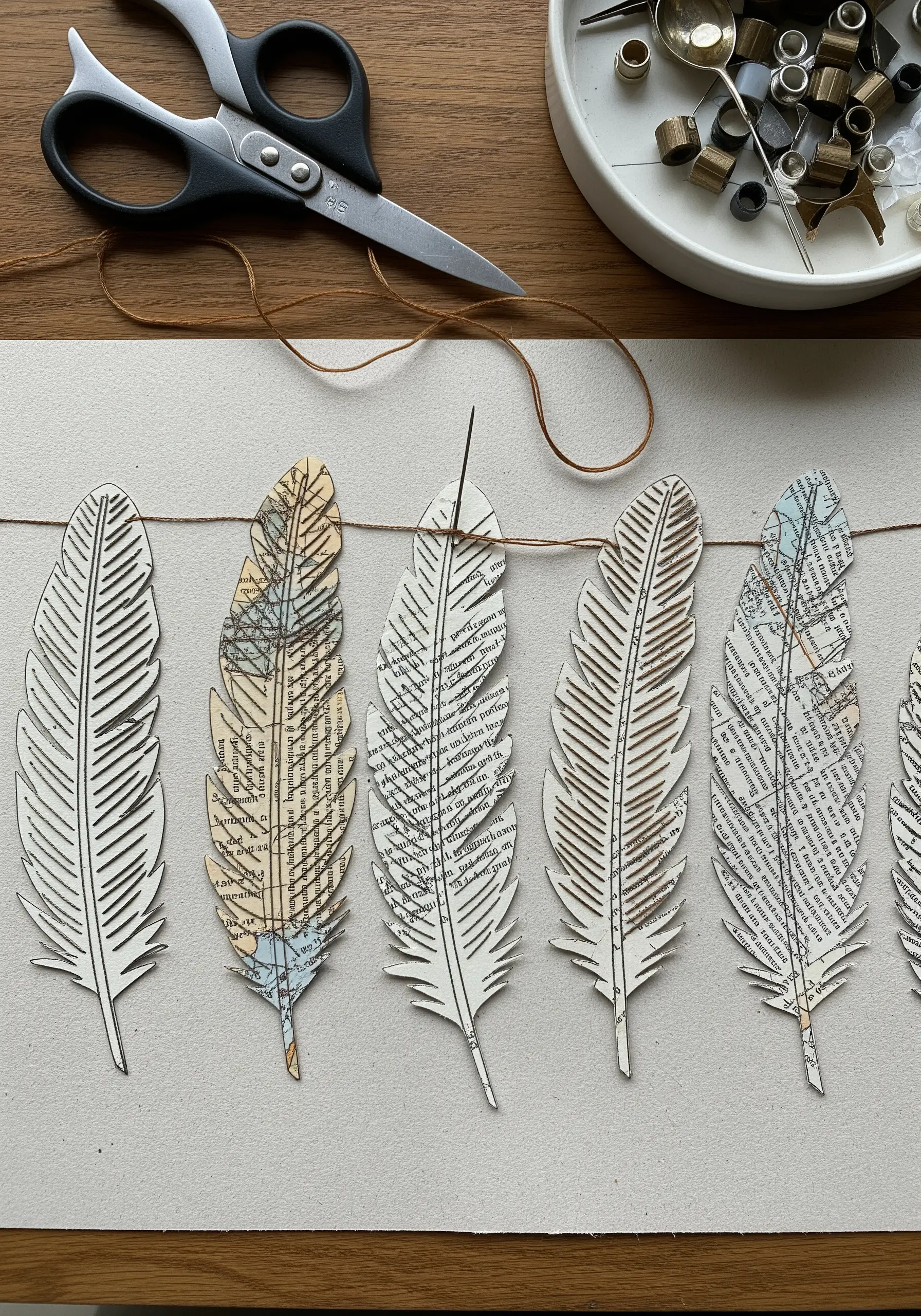 A garland of paper feathers cut from maps and book pages, with stitched details along the spine.