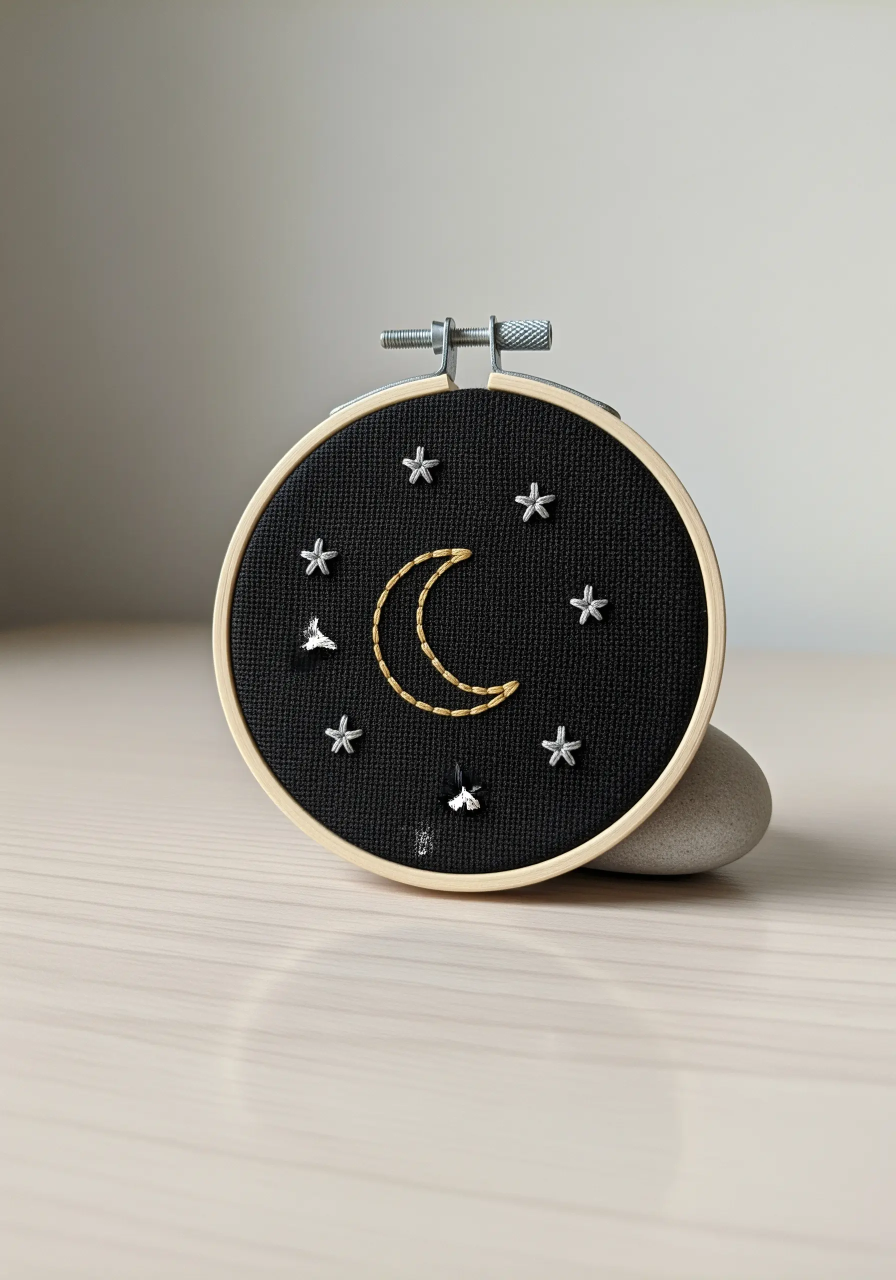 A small embroidered crescent moon and stars in gold and silver on black Aida cloth.