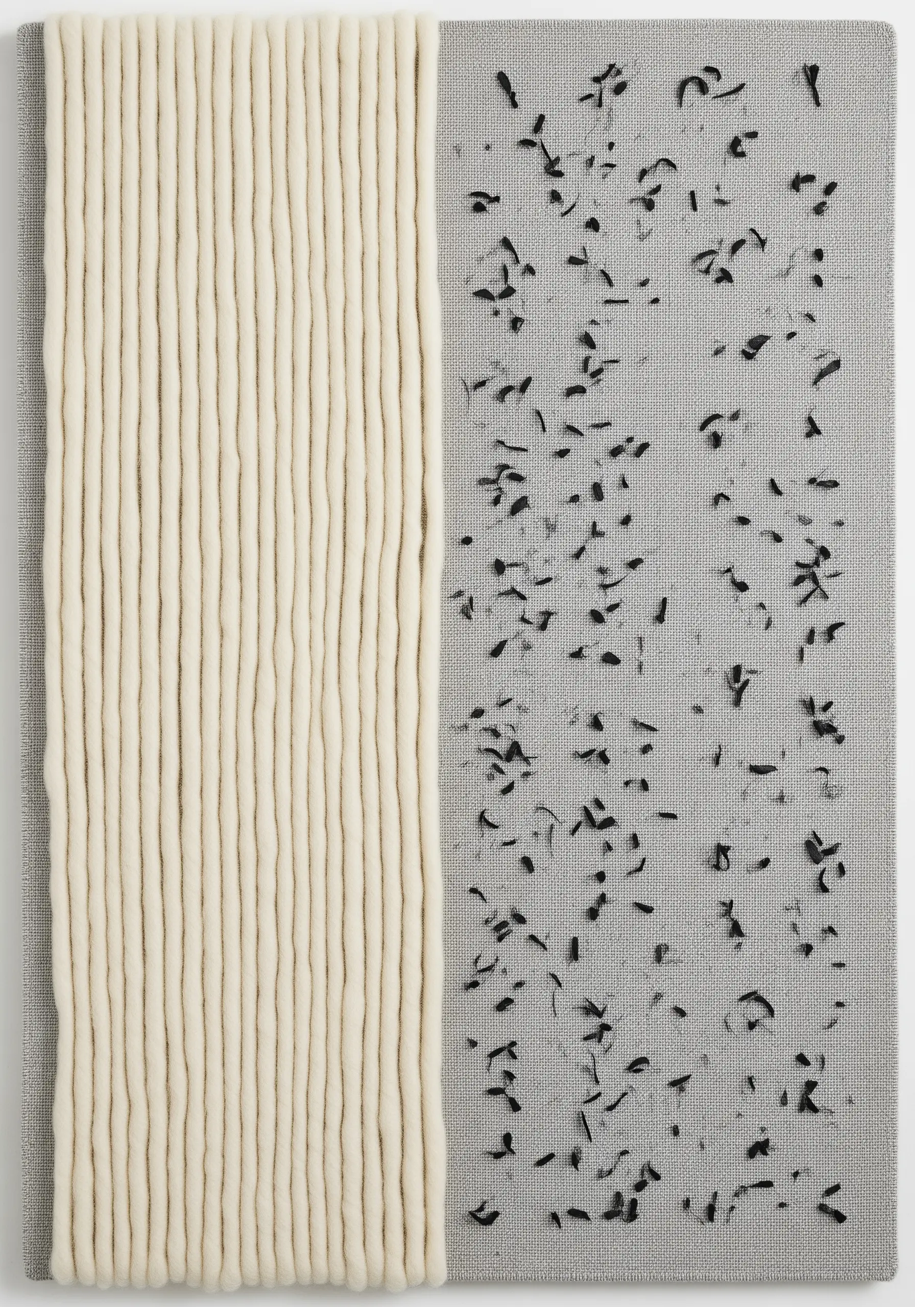 Thick vertical strands of cream-colored wool roving next to scattered, small black stitches on gray canvas.