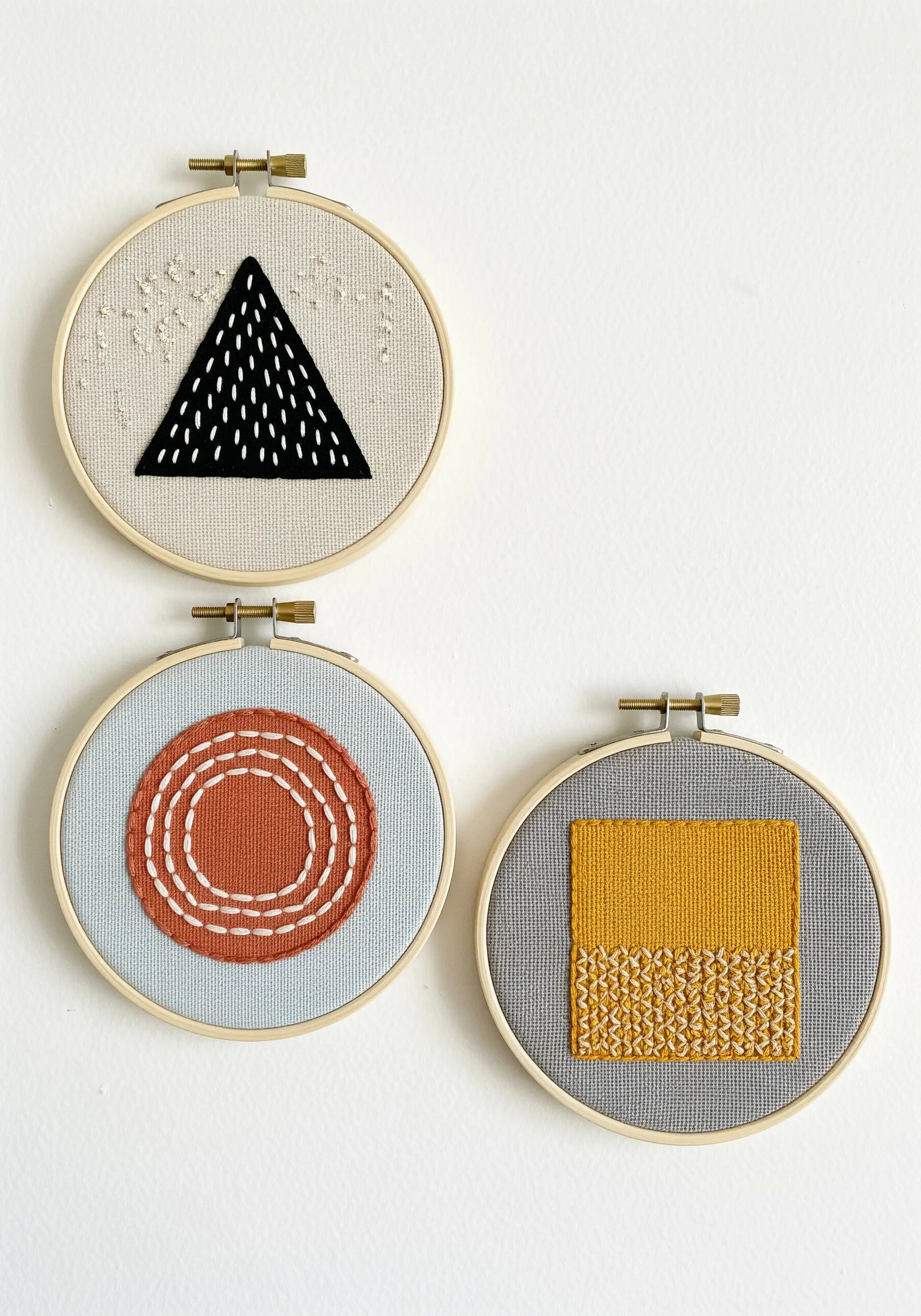A set of three embroidery hoops with abstract geometric shapes filled with different stitch textures.