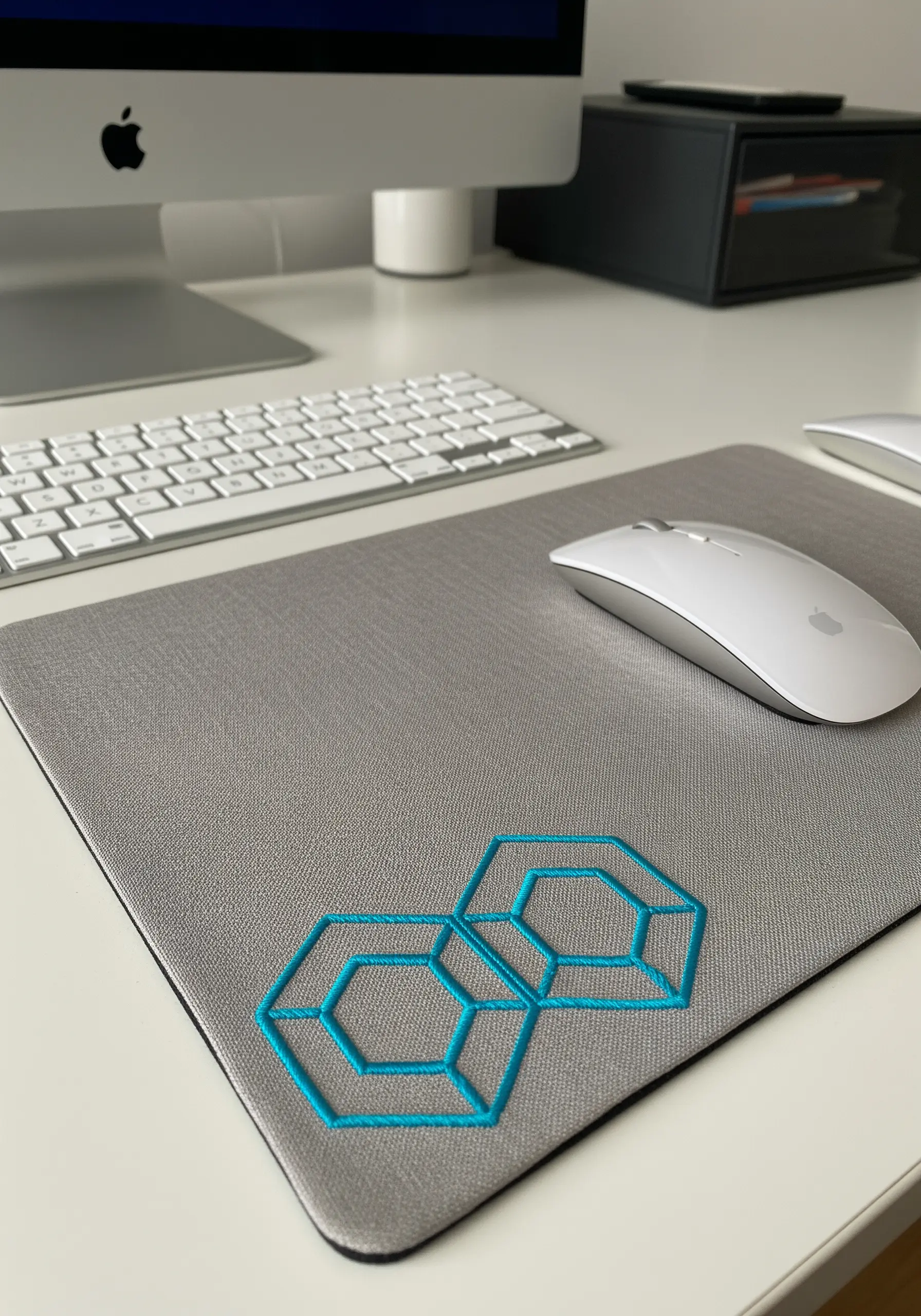 A grey mousepad on a white desk, embroidered with a bright blue geometric honeycomb pattern.