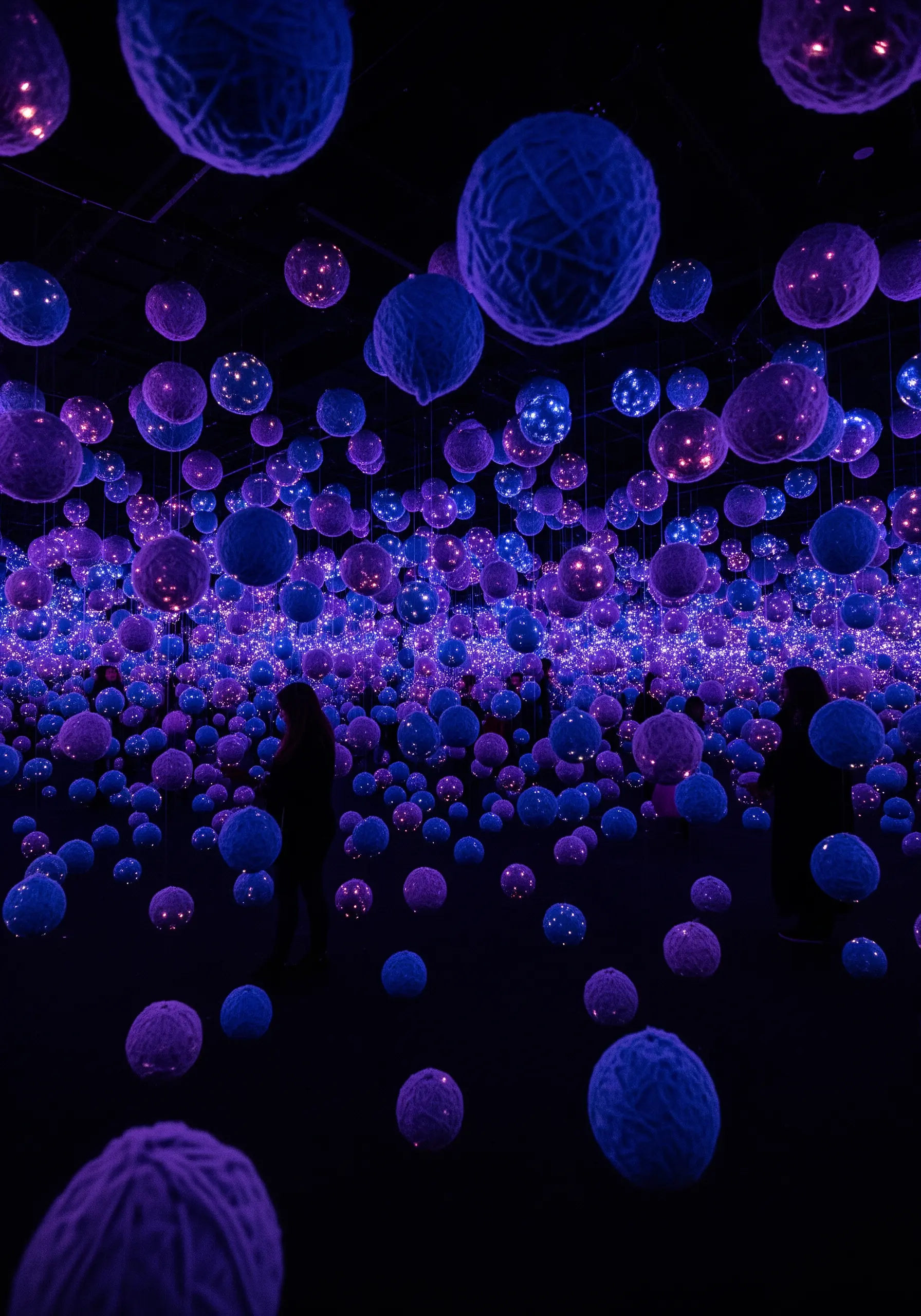 A dark room filled with glowing purple and blue spheres of yarn hanging from the ceiling.