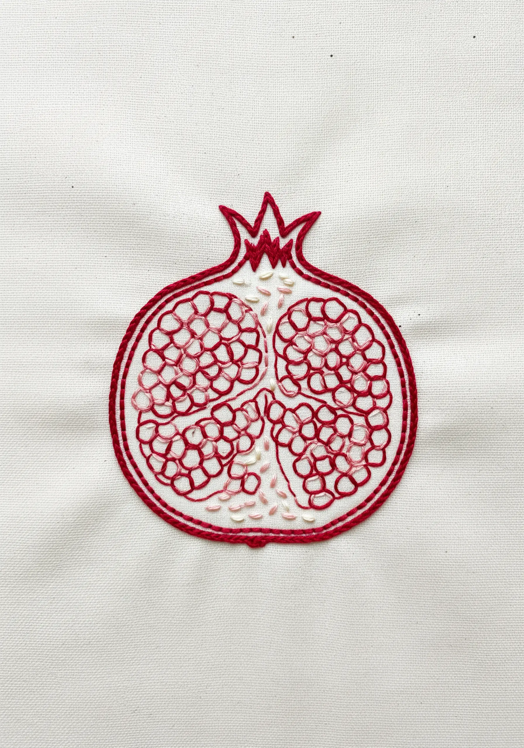 An embroidered cross-section of a pomegranate using red outlines and scattered seed stitches.
