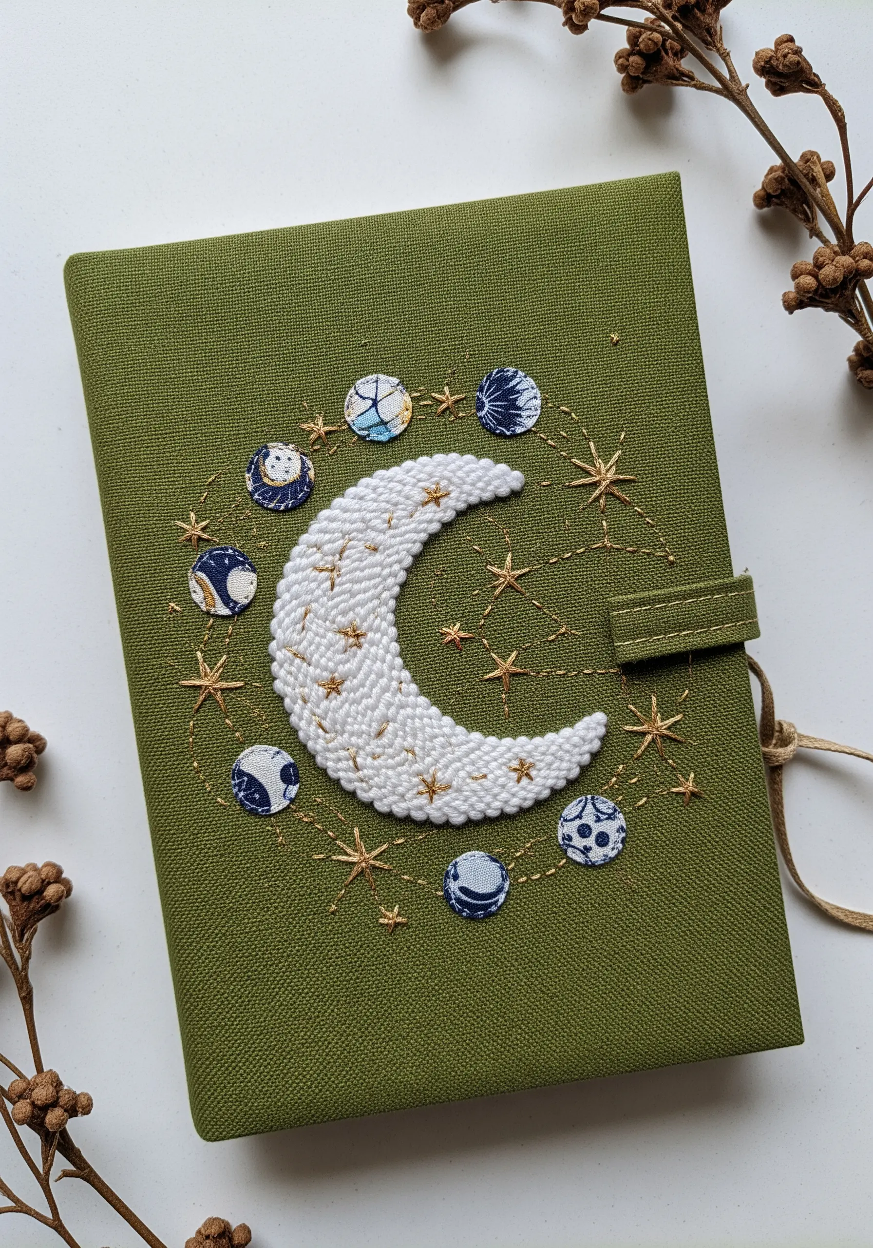 An olive green journal cover with an embroidered crescent moon and appliqué fabric moon phases.
