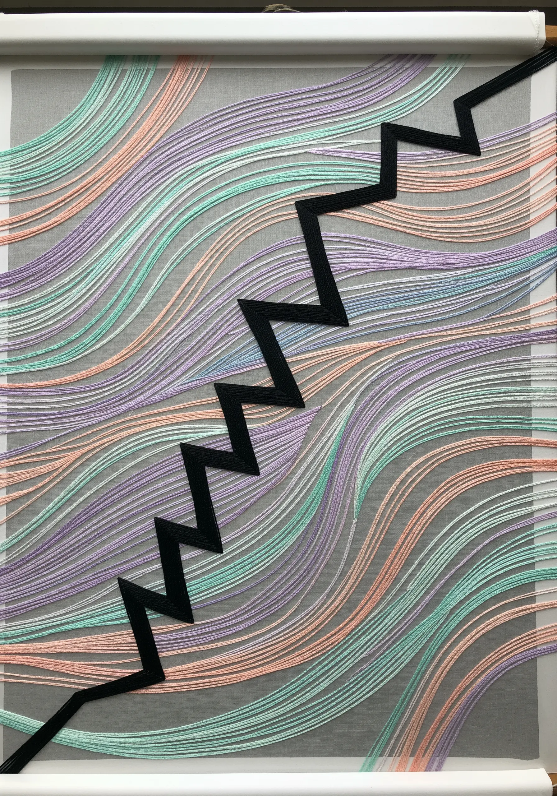 A sharp, black zig-zag ribbon stitched over a soft, flowing background of pastel threads.