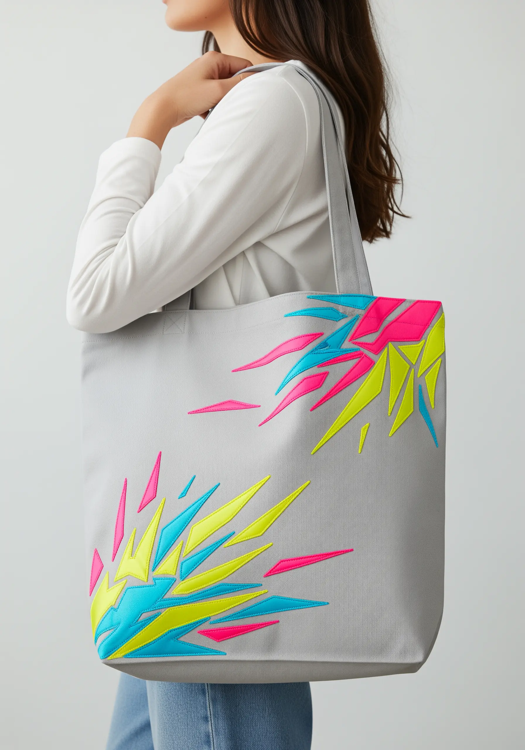 Abstract geometric bursts of neon pink, yellow, and blue embroidery on a grey tote bag.