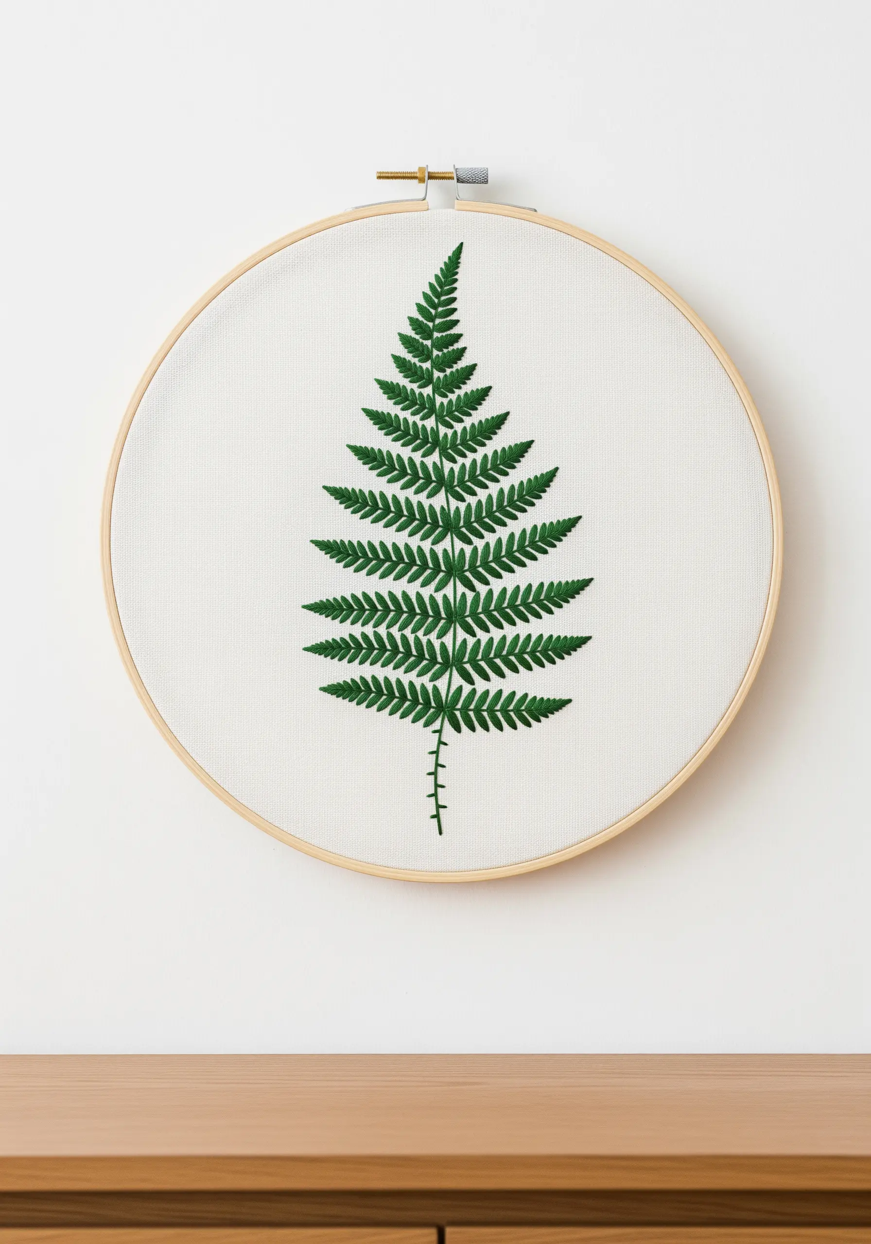 A single green fern embroidered in a wooden hoop using fishbone stitch.