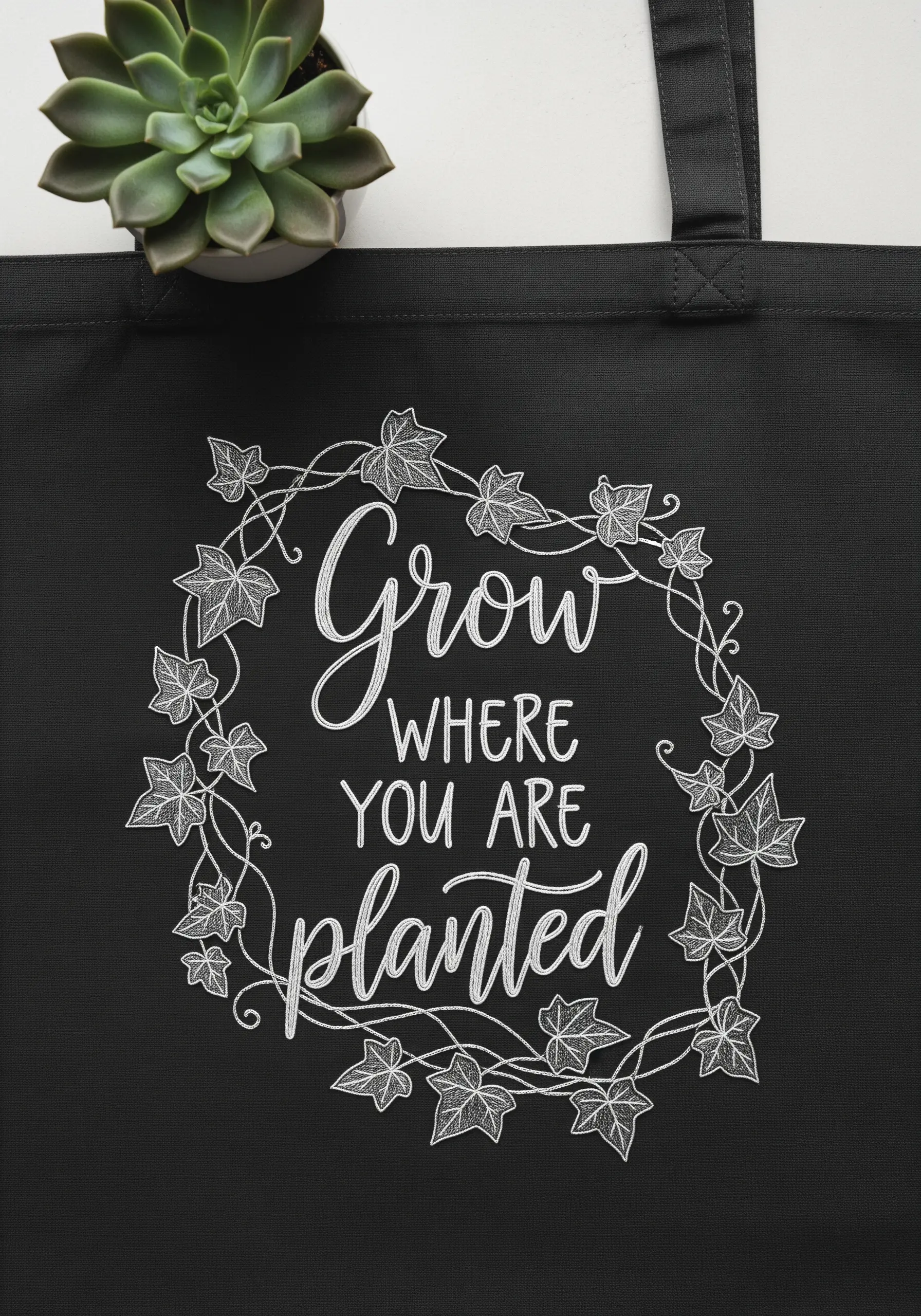 Black tote bag featuring a delicate white embroidery of an ivy wreath and script.