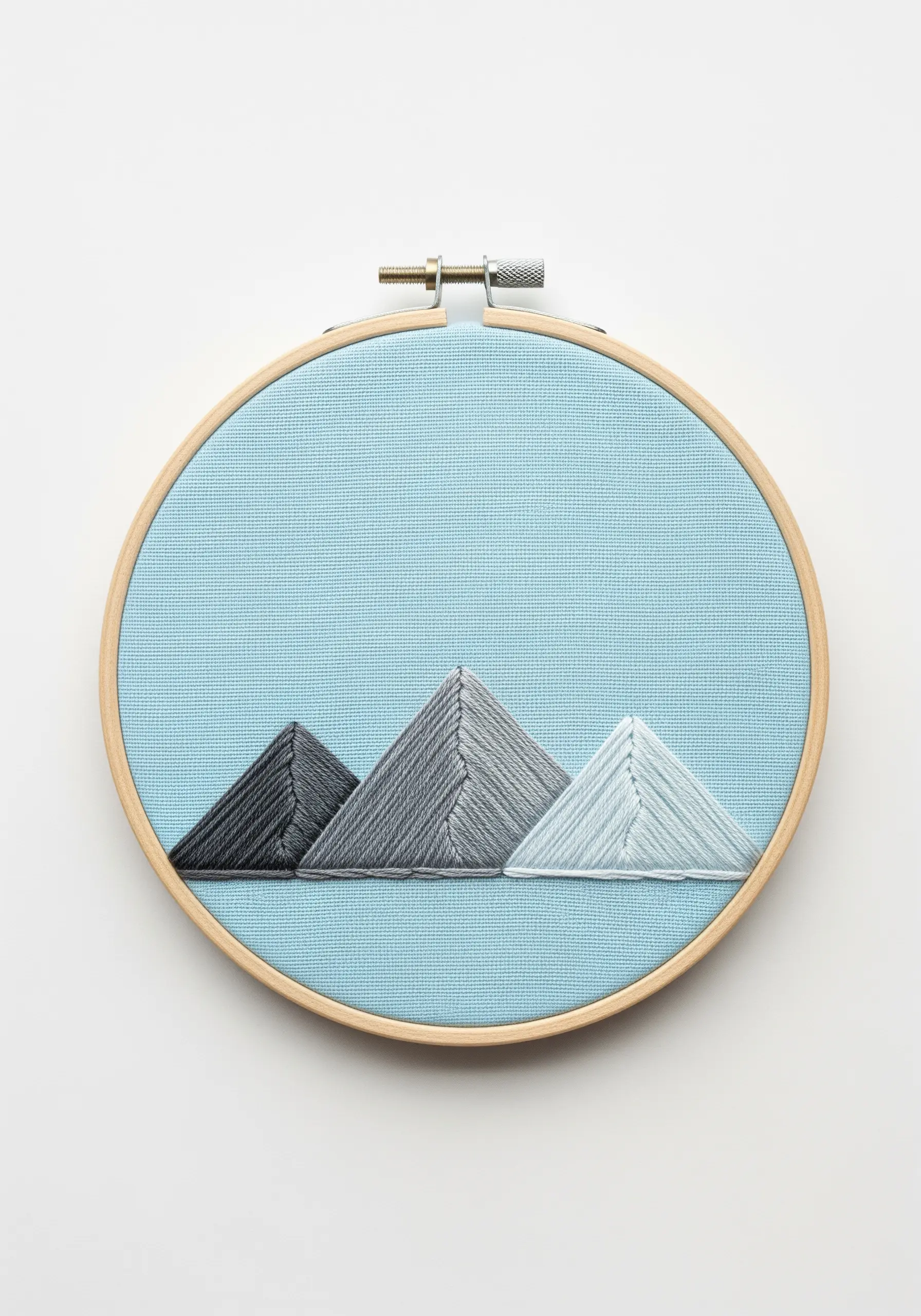 Three embroidered mountains in a grayscale gradient against a light blue fabric background.