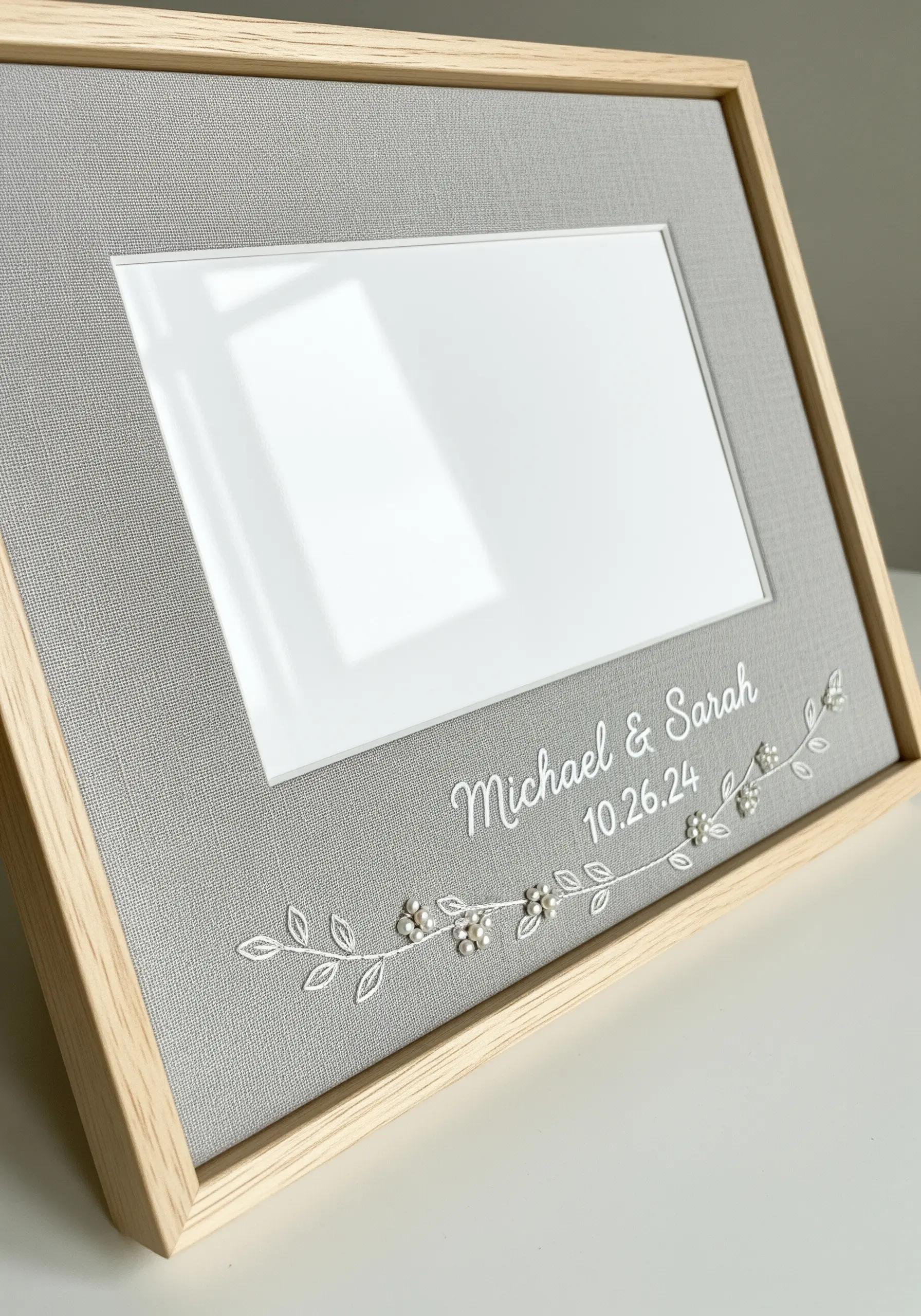 A gray photo frame mat embroidered with names, a date, and delicate vines with pearls.