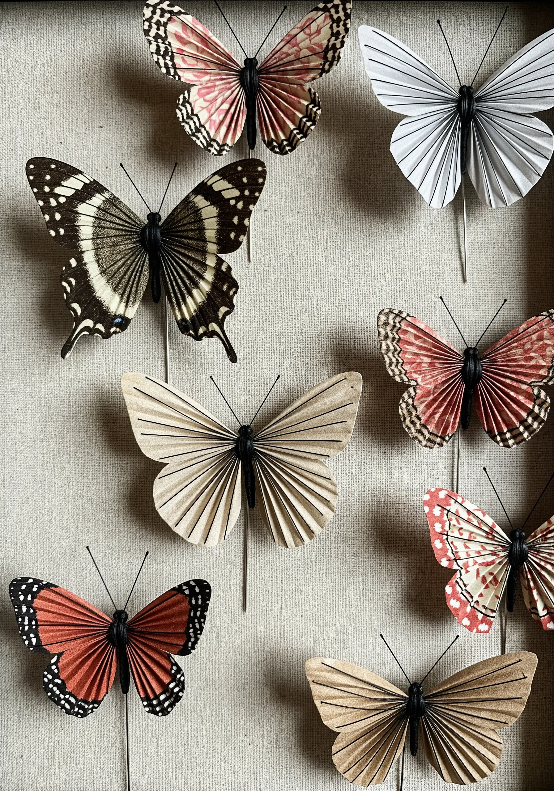 A collection of 3D paper butterflies with patterned and pleated wings and black thread bodies.