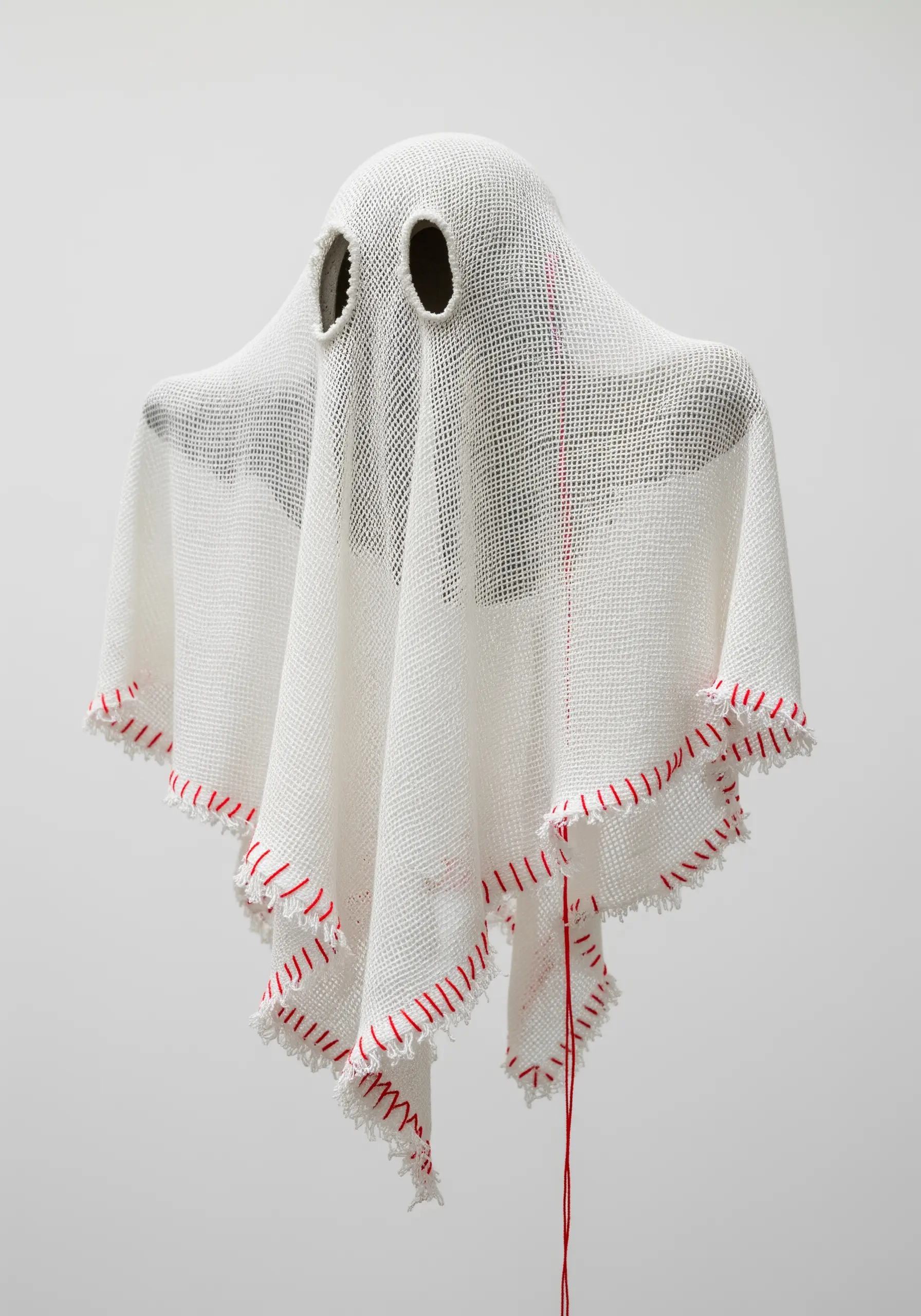 A draped white ghost-like sculpture made from stiffened fabric with red stitched edges.