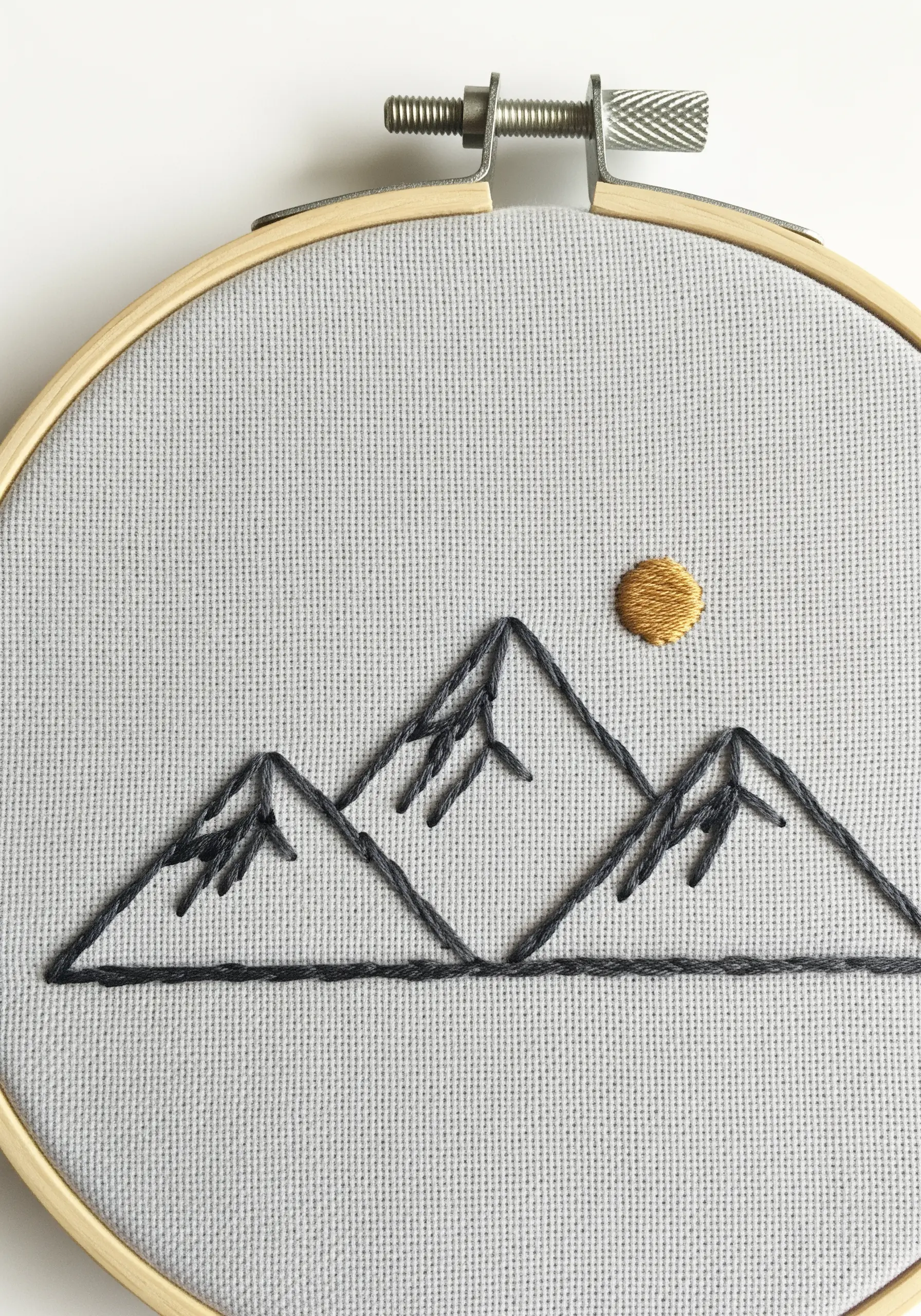 Minimalist line art embroidery of mountains and a golden sun.