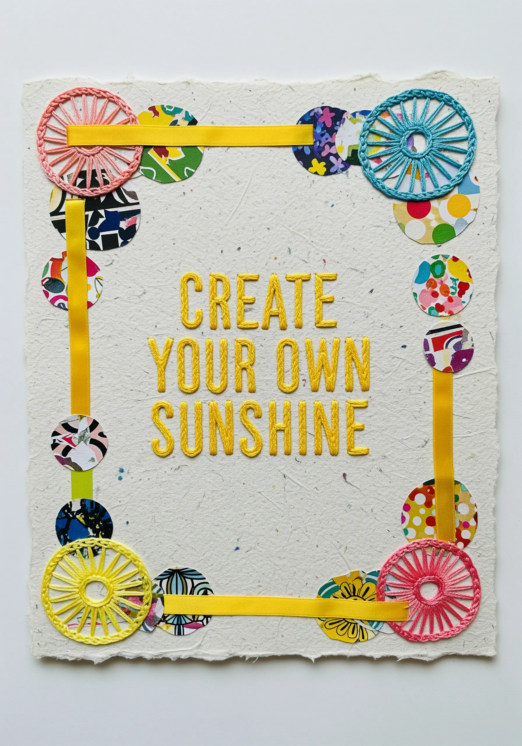 An inspirational quote stitched on handmade paper, framed with ribbon and colorful paper circles.