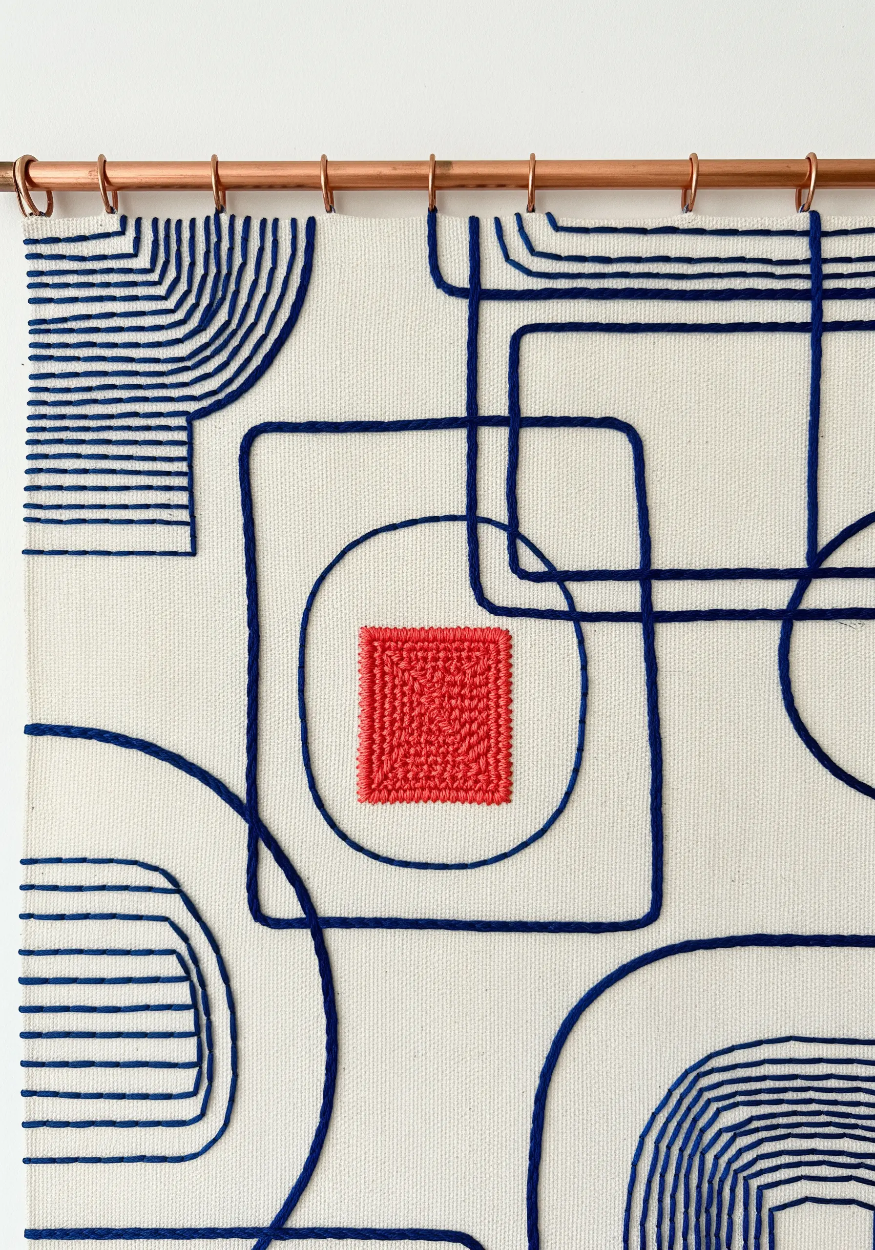 A modern wall hanging with blue line art and a single, densely stitched red square as a focal point.