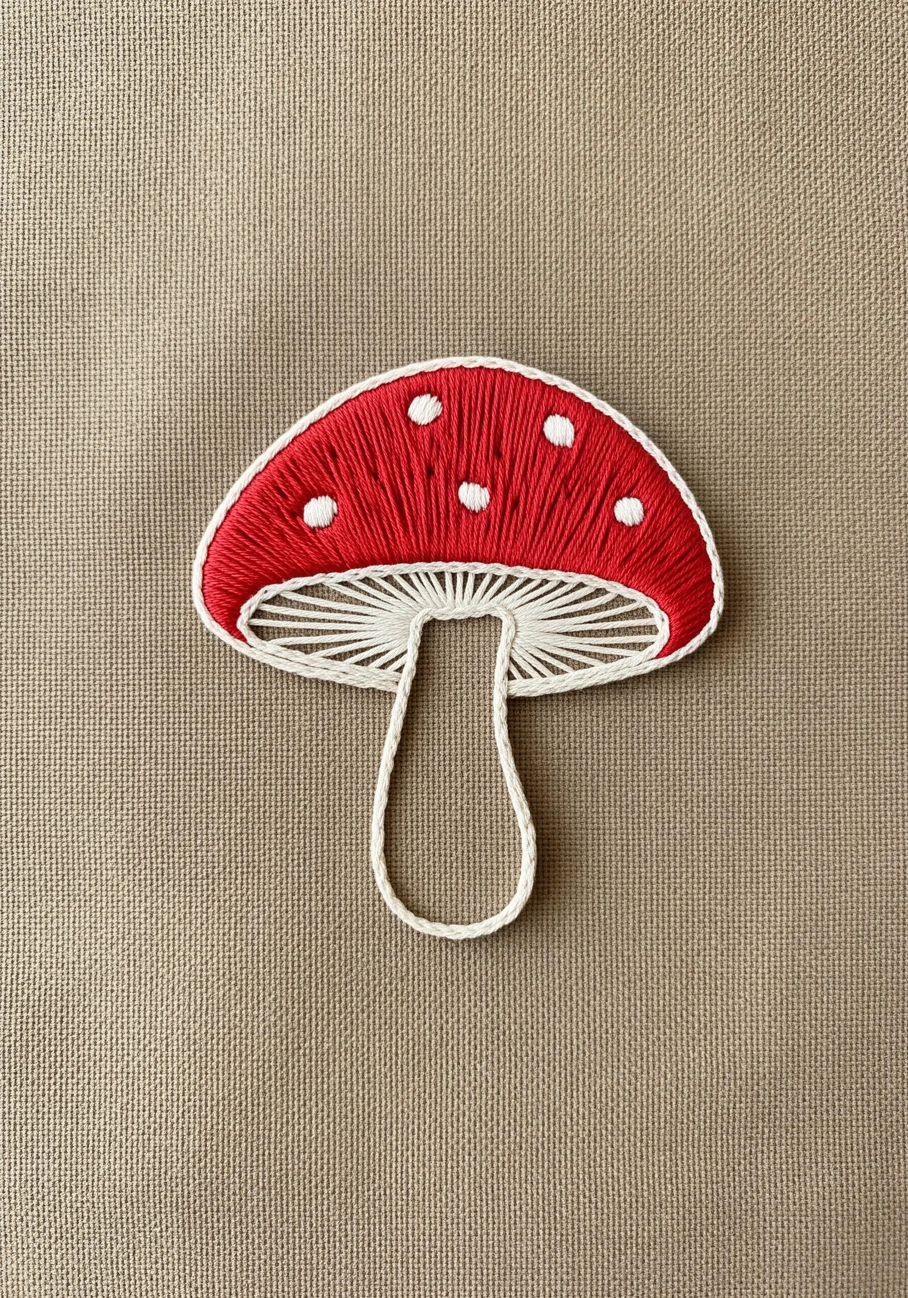 A red-and-white toadstool mushroom embroidered with directional satin and straight stitches.