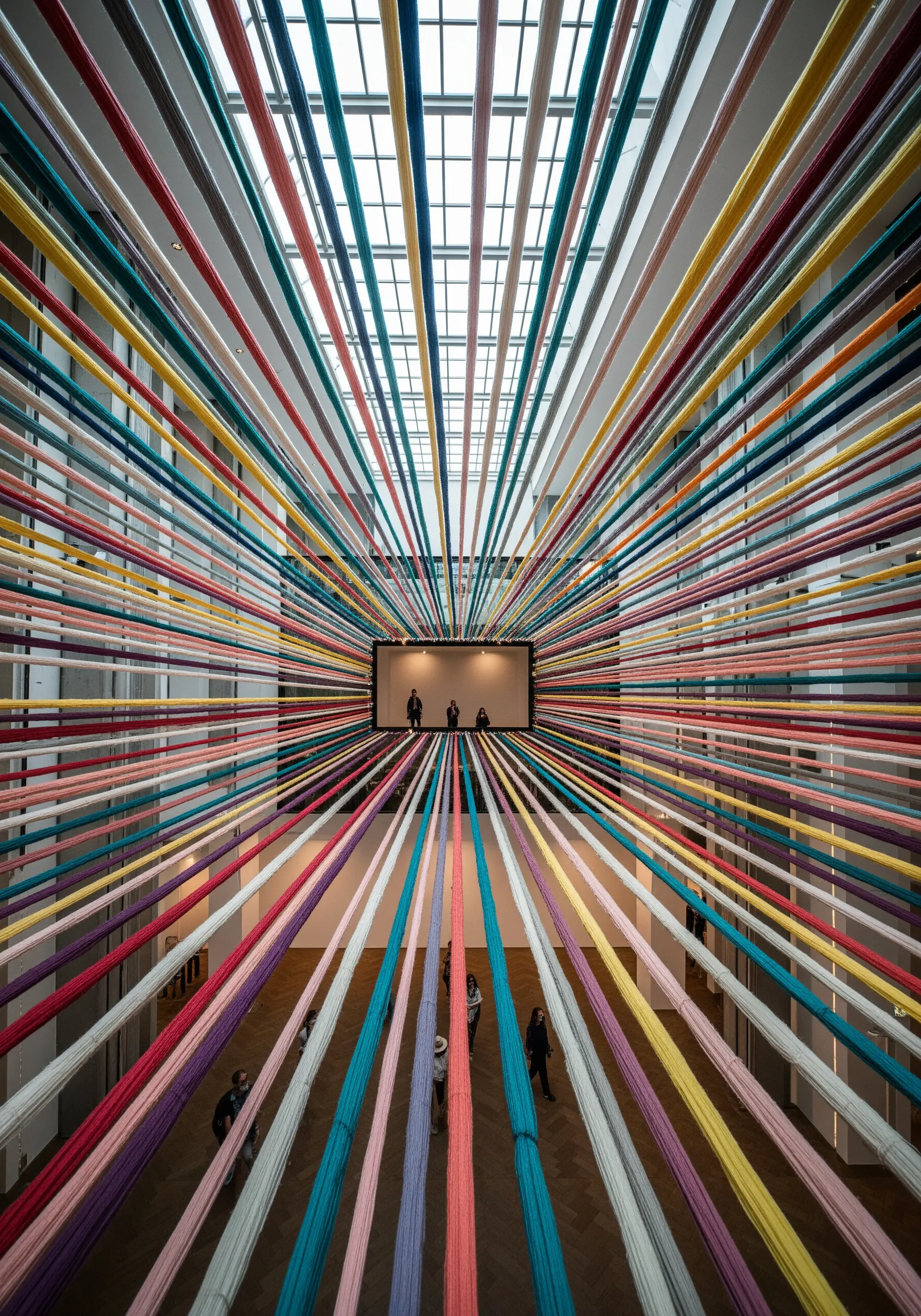 Colorful threads stretched across a room from floor to ceiling, creating a perspective tunnel.