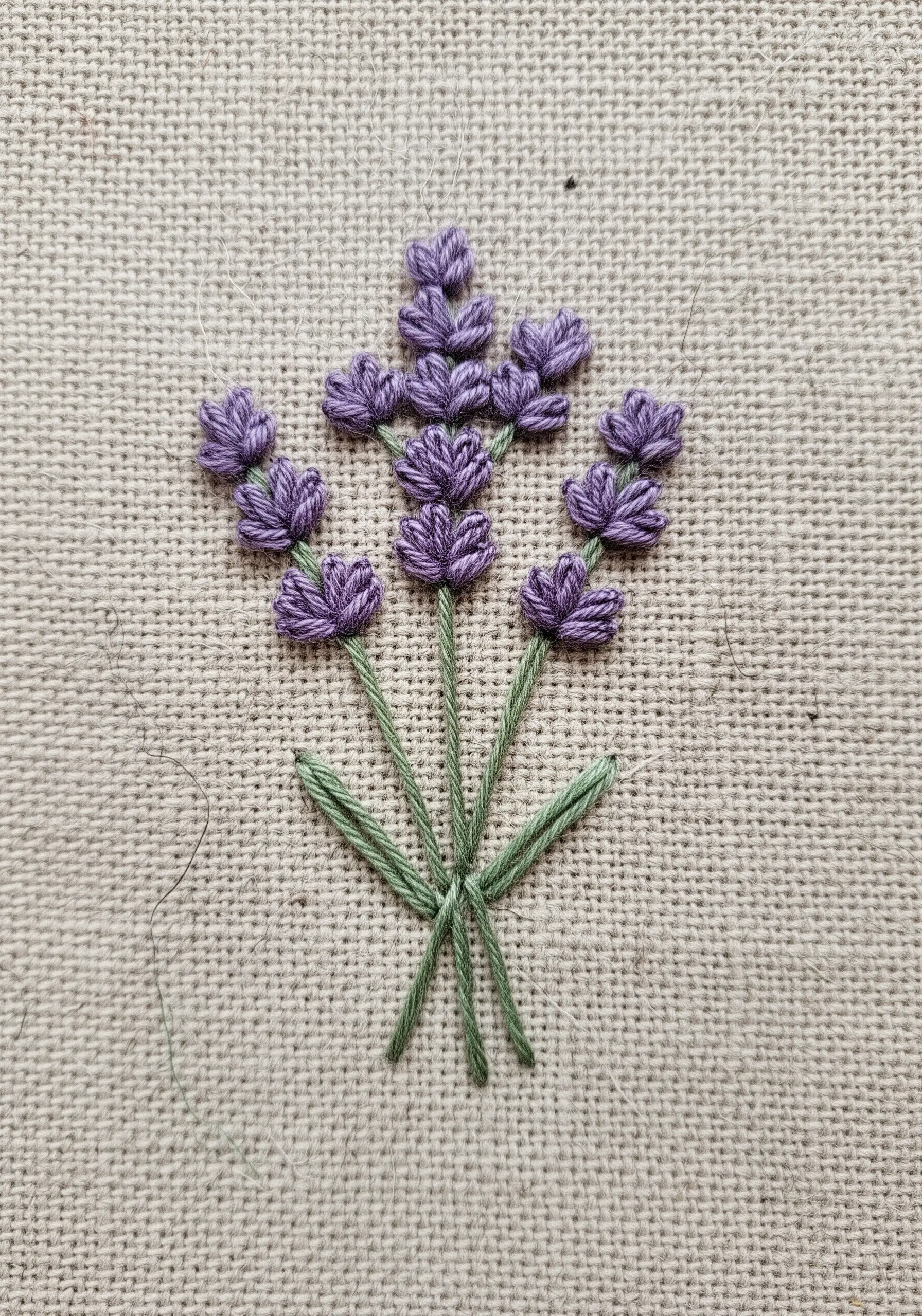 A small bouquet of embroidered lavender with textured purple buds and green stems.
