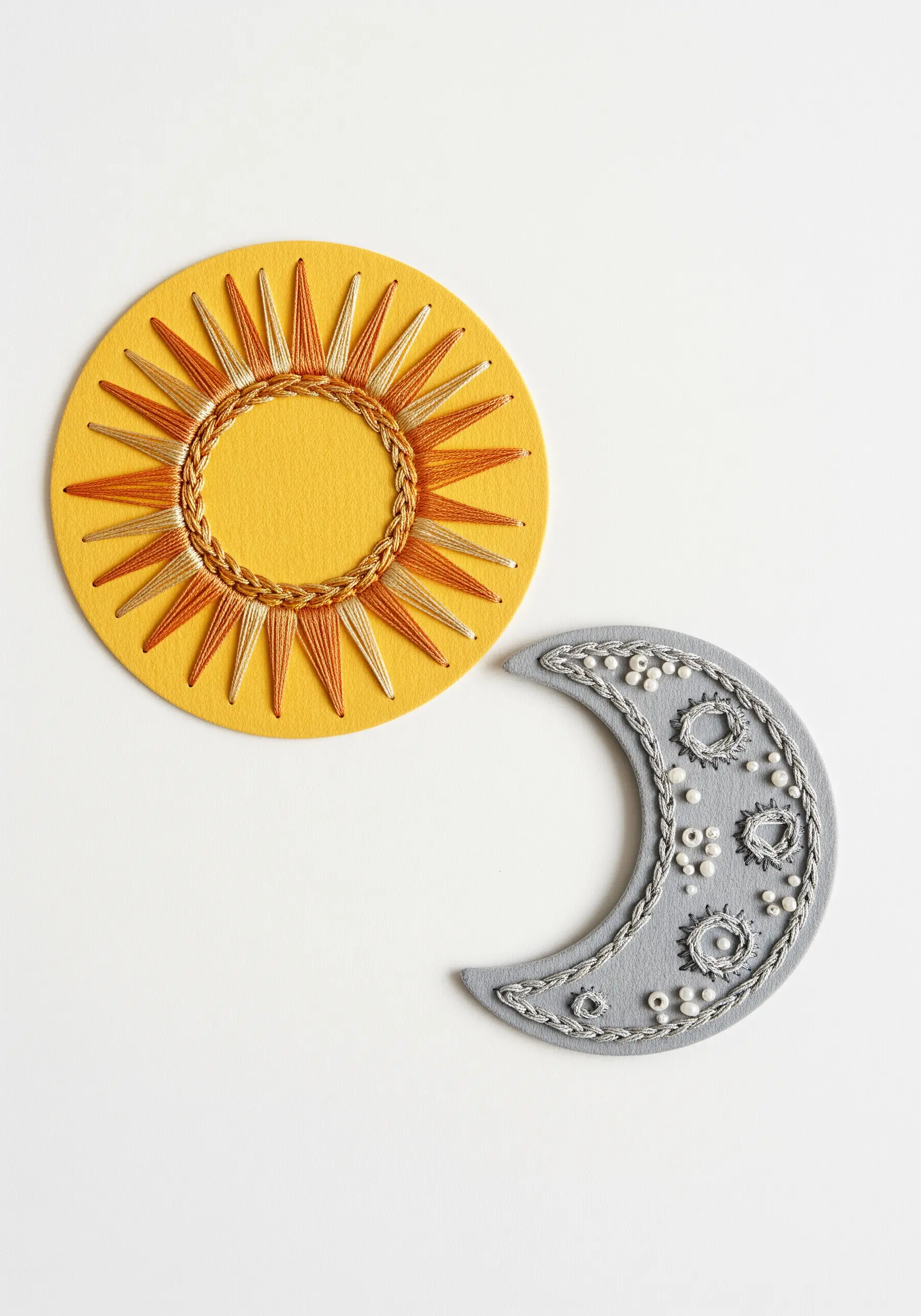 An embroidered sun with blended orange and gold thread, and a gray moon with silver thread and beads.
